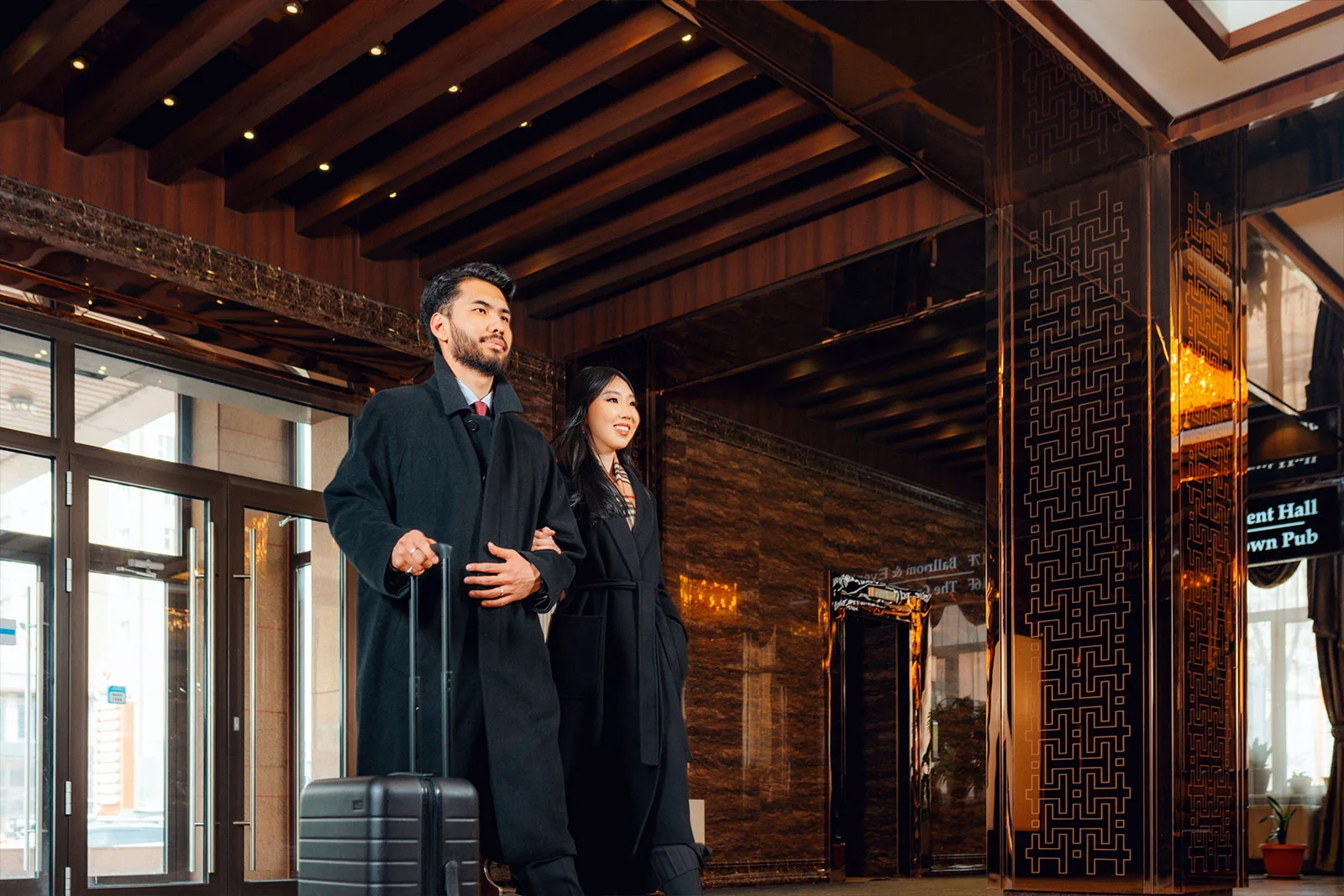 Representative hotel space: A couple stands with luggage in a hotel lobby with dark wood beams.