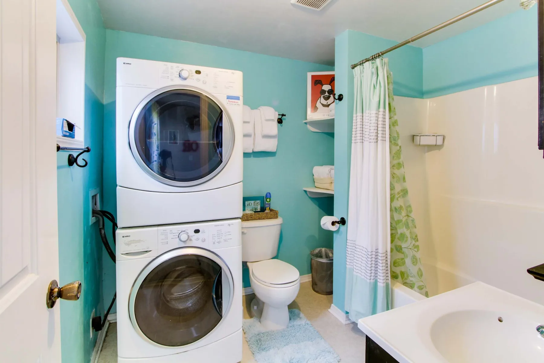 A bathroom with a stacked washer and dryer beside a bathtub and sink.