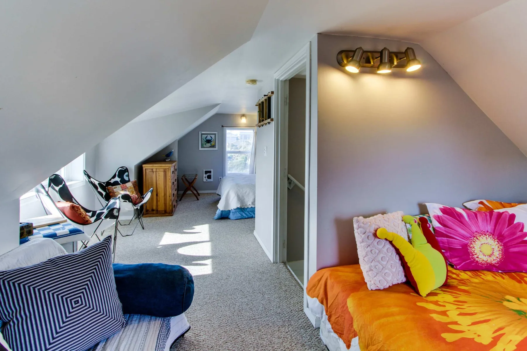 A bright attic bedroom with colorful bedding and a small desk area.