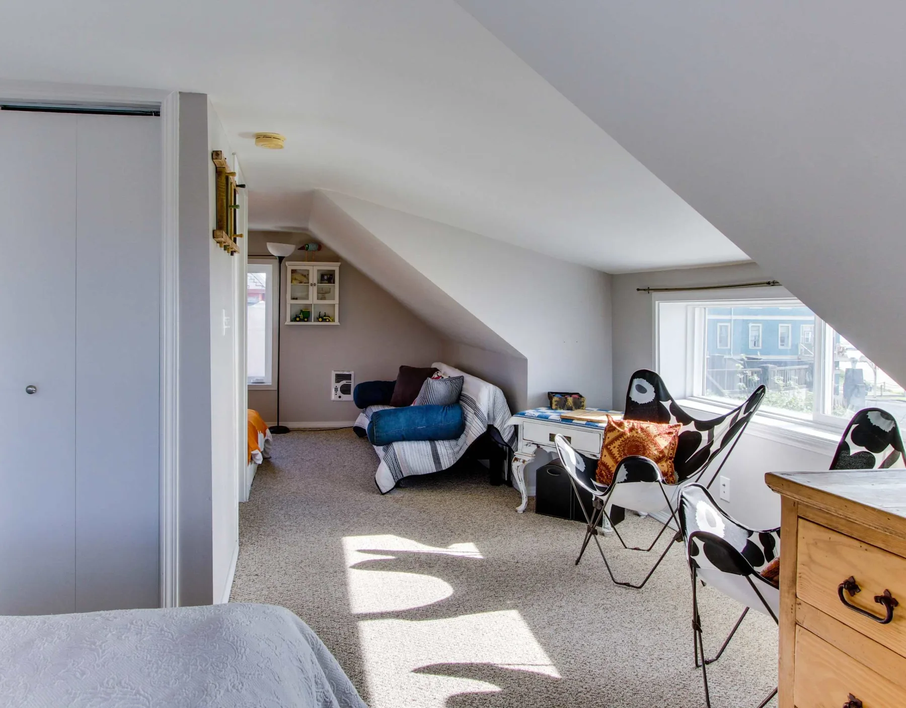 A bright attic room with seating, a small table, and large windows.