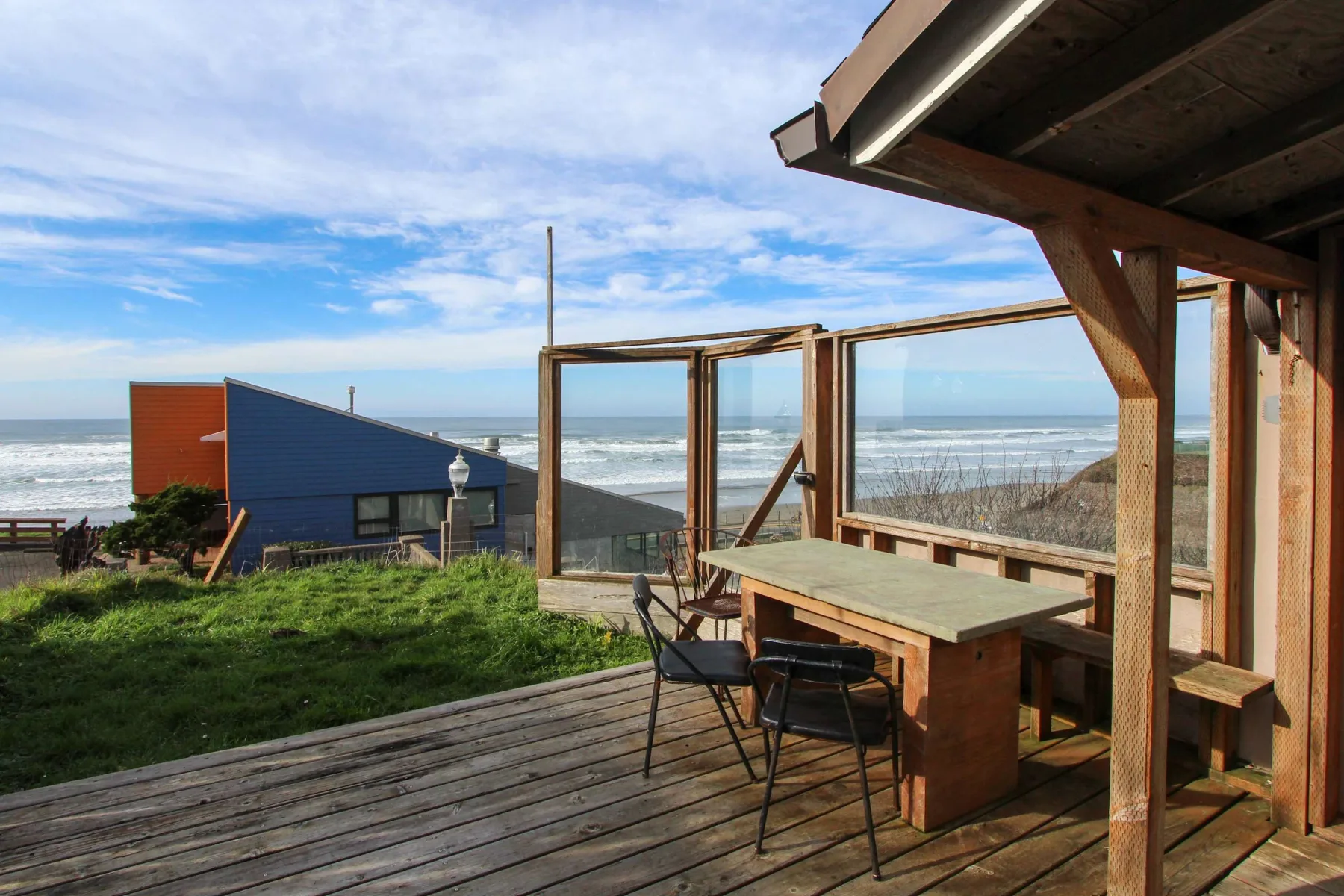 A wooden deck with a table and seating overlooks the ocean.