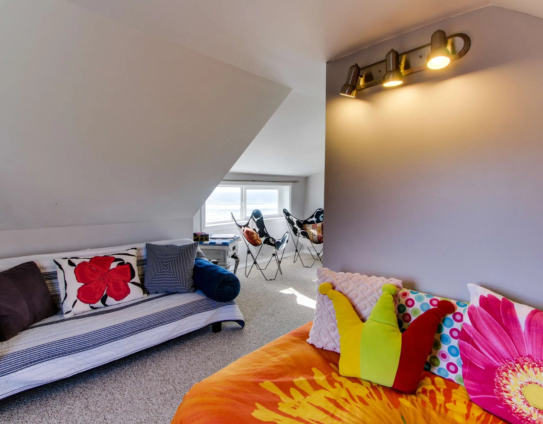 A colorful attic lounge has floor seating and chairs beside a window.