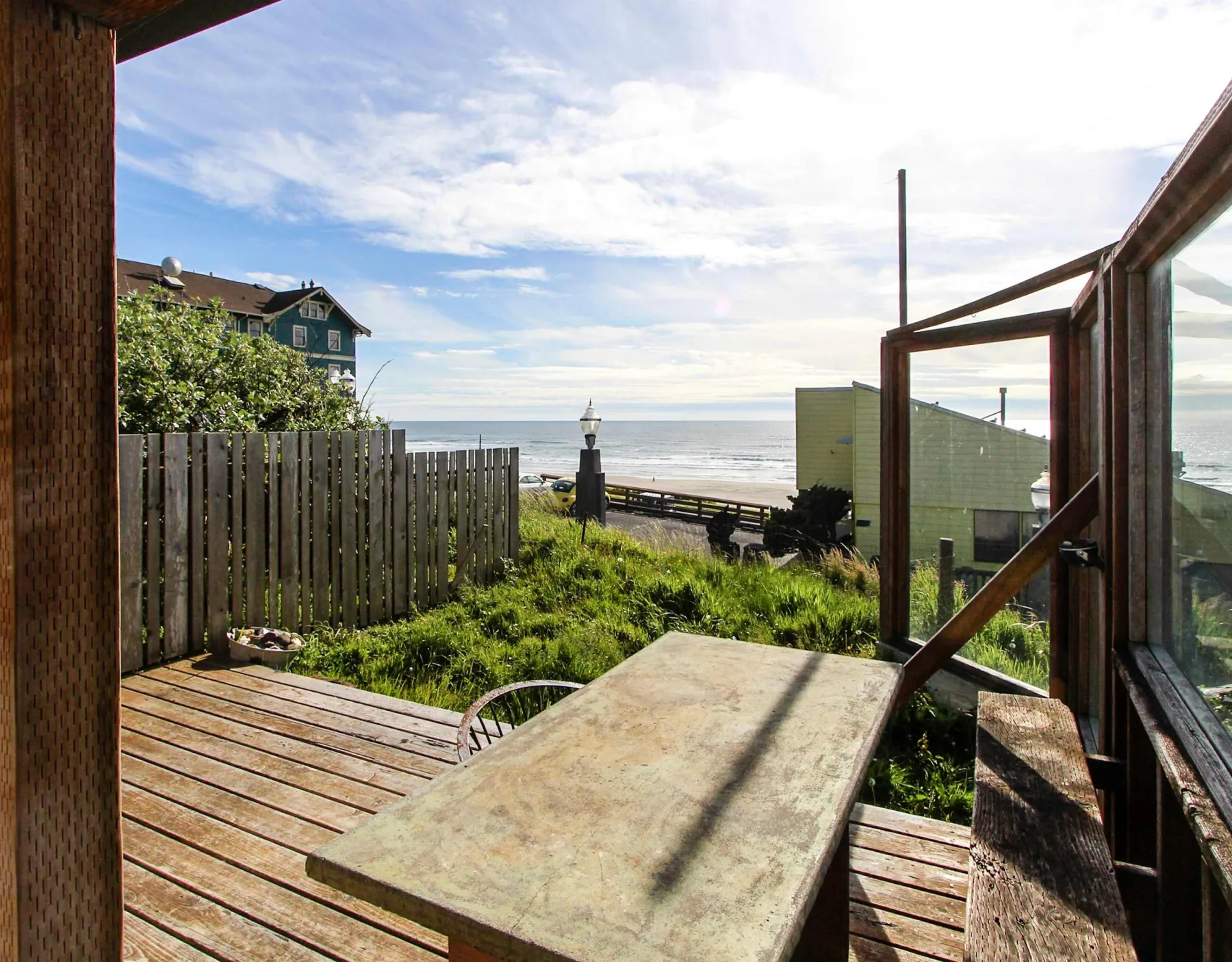 A wooden deck with a table overlooks grassy ground and the ocean.