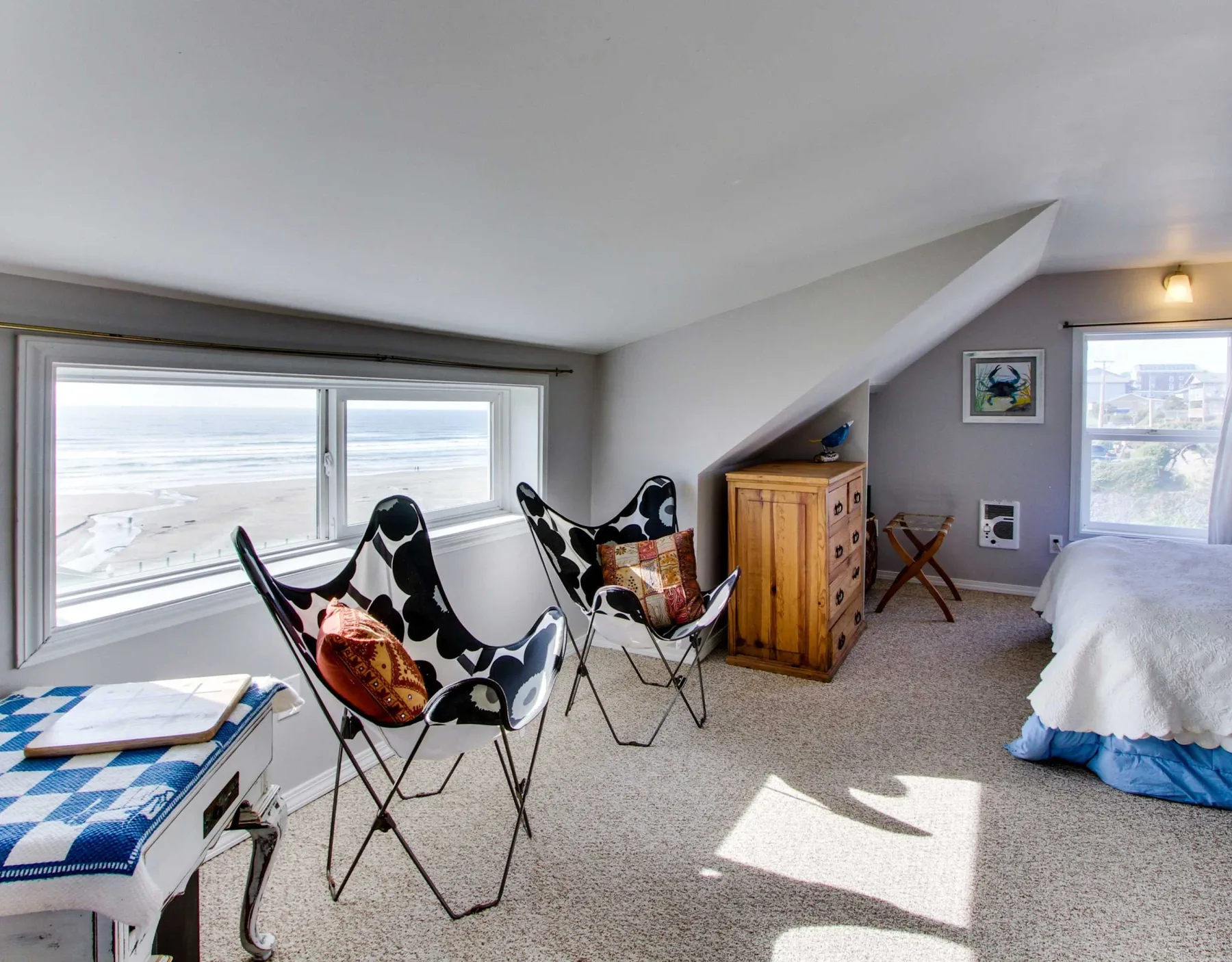 A bright attic bedroom with seating beside wide windows and a bed.