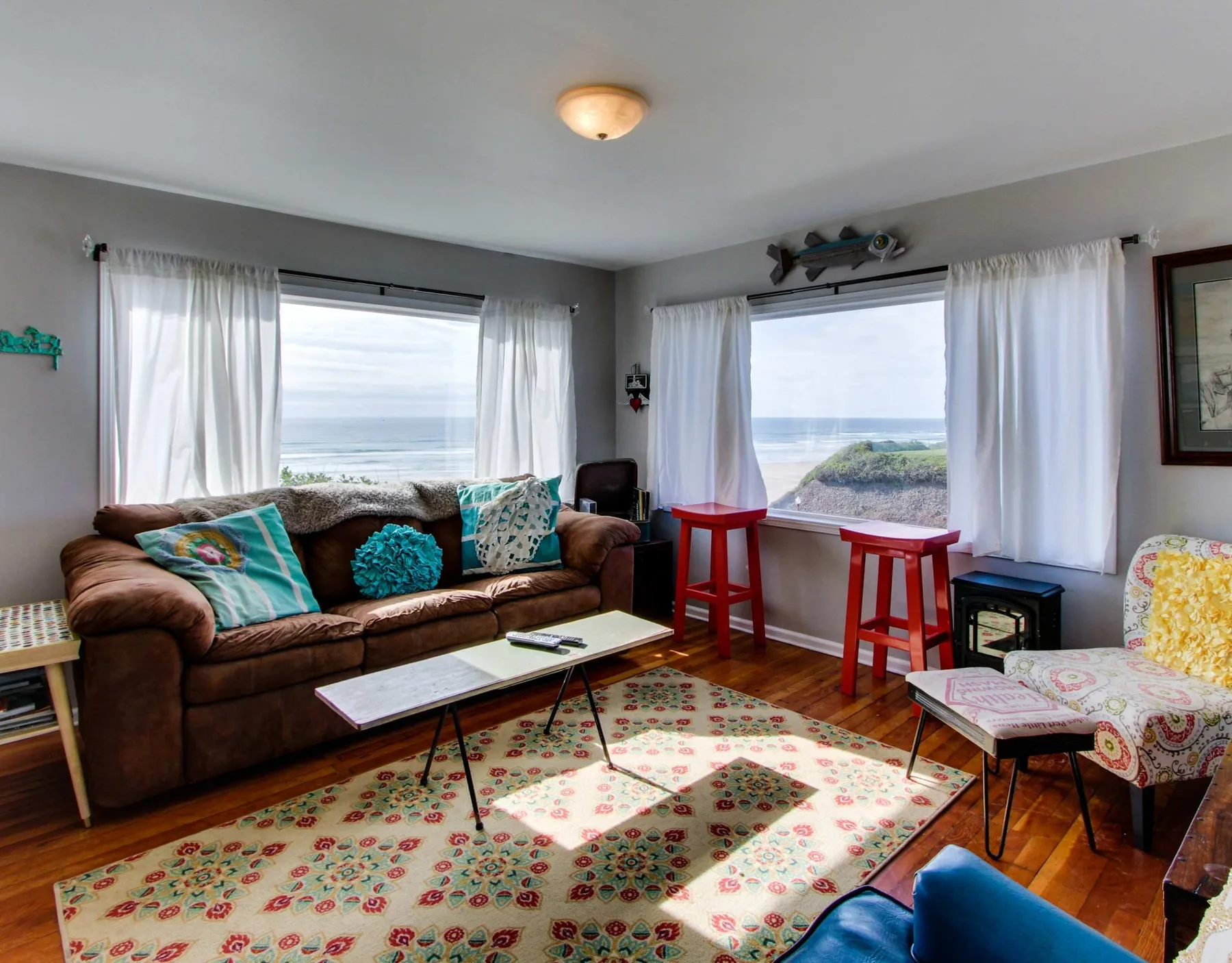 A living room with a brown sofa, colorful rug, and windows overlooking the water.