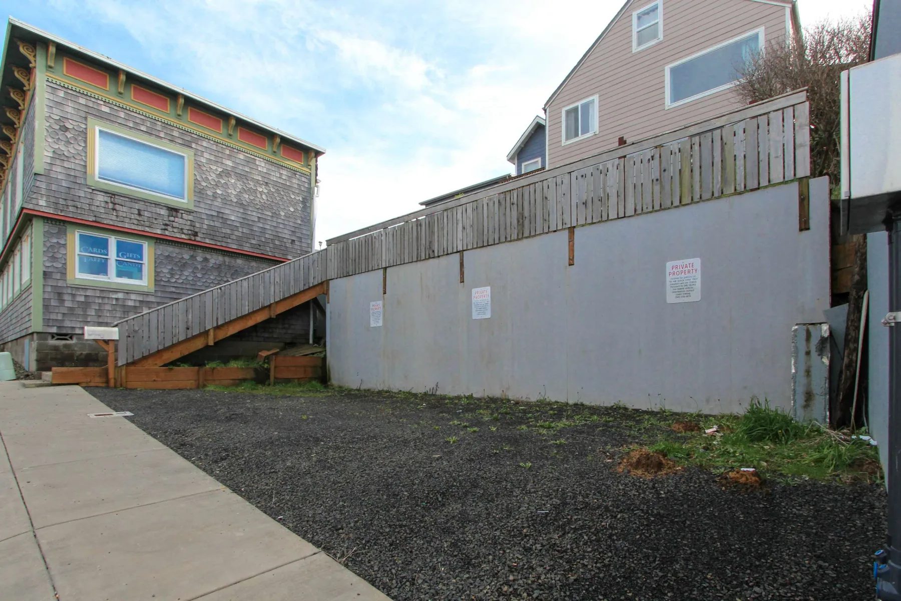 An outdoor walkway runs beside a tall fence between buildings.