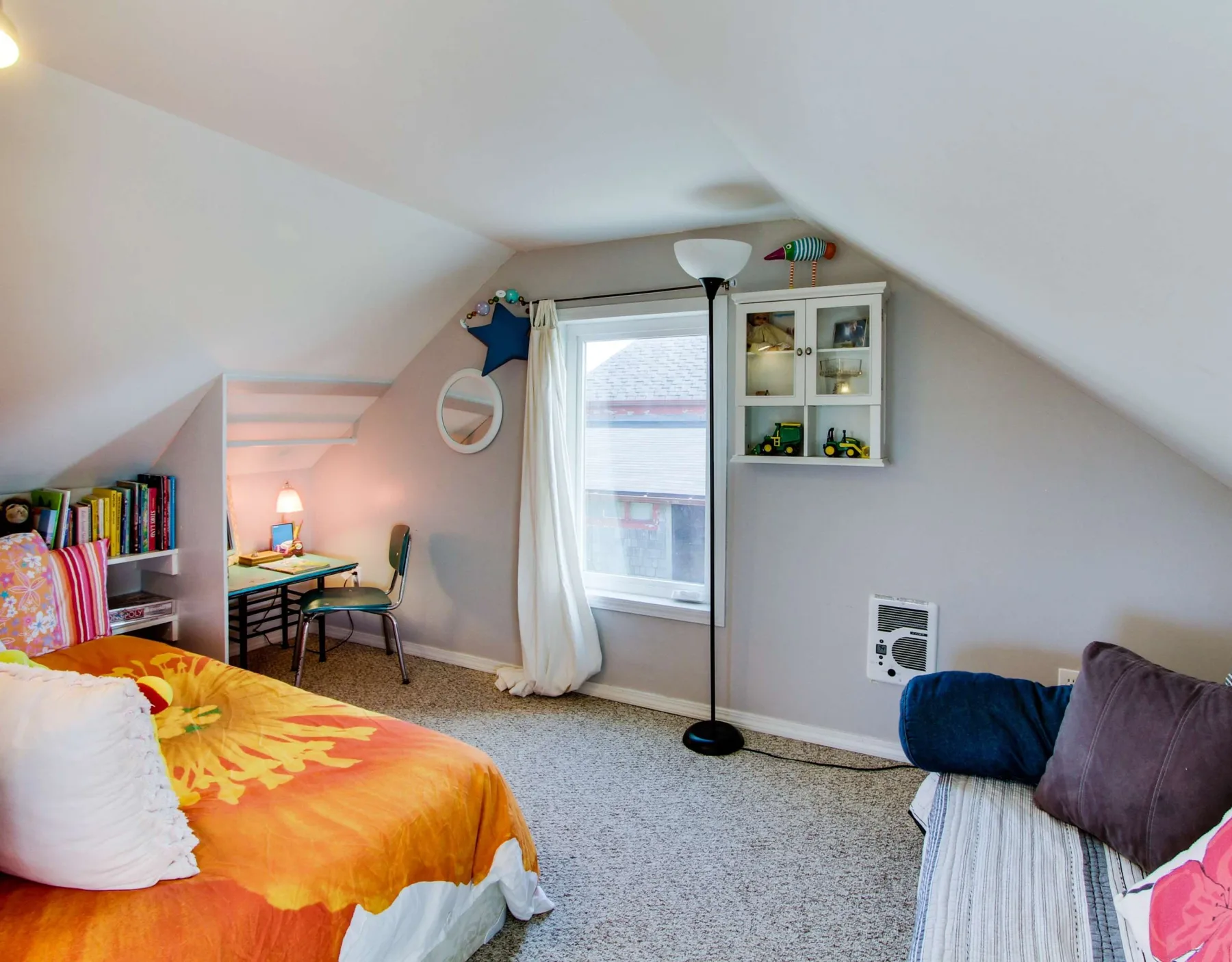A carpeted bedroom with a bed, desk, and window beneath a sloped ceiling.
