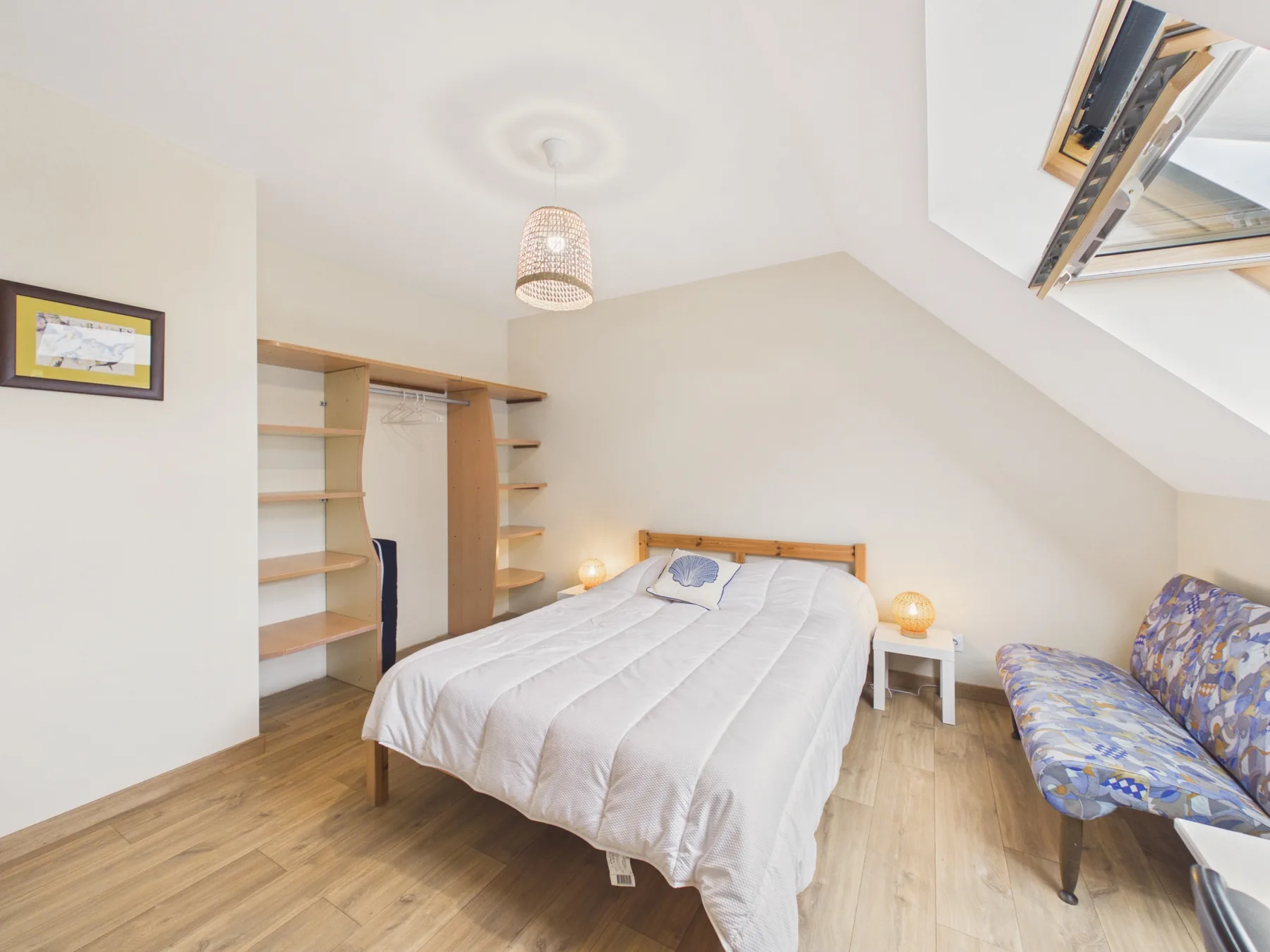 A bedroom with a double bed and a patterned seating area beneath a sloped ceiling.