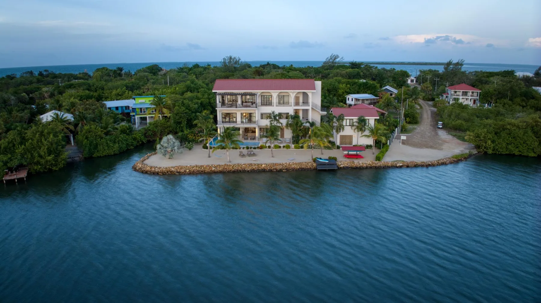 A waterfront building and nearby homes sit among greenery beside the water.