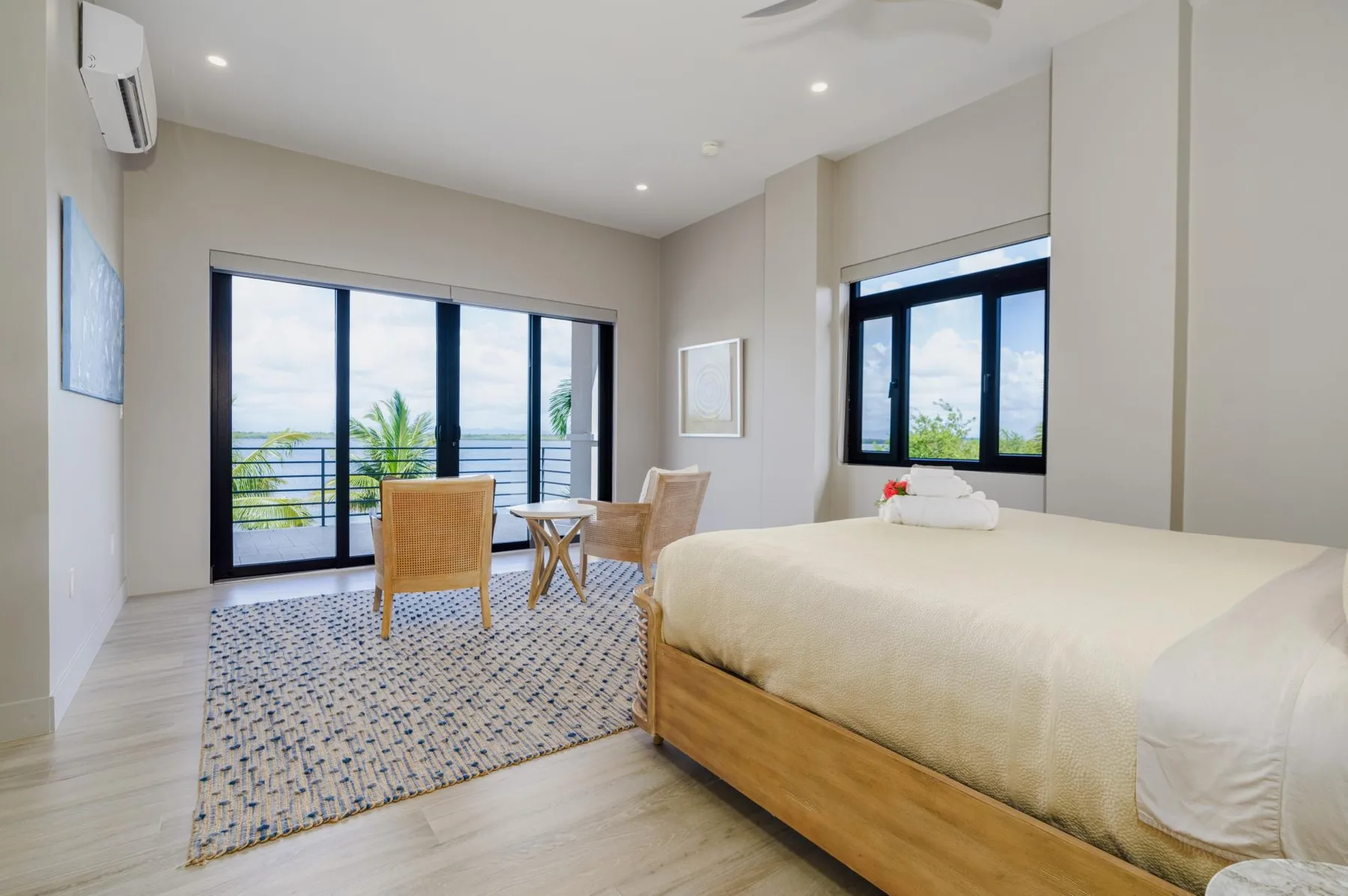 A bright bedroom with a large bed, seating, and windows overlooking greenery.