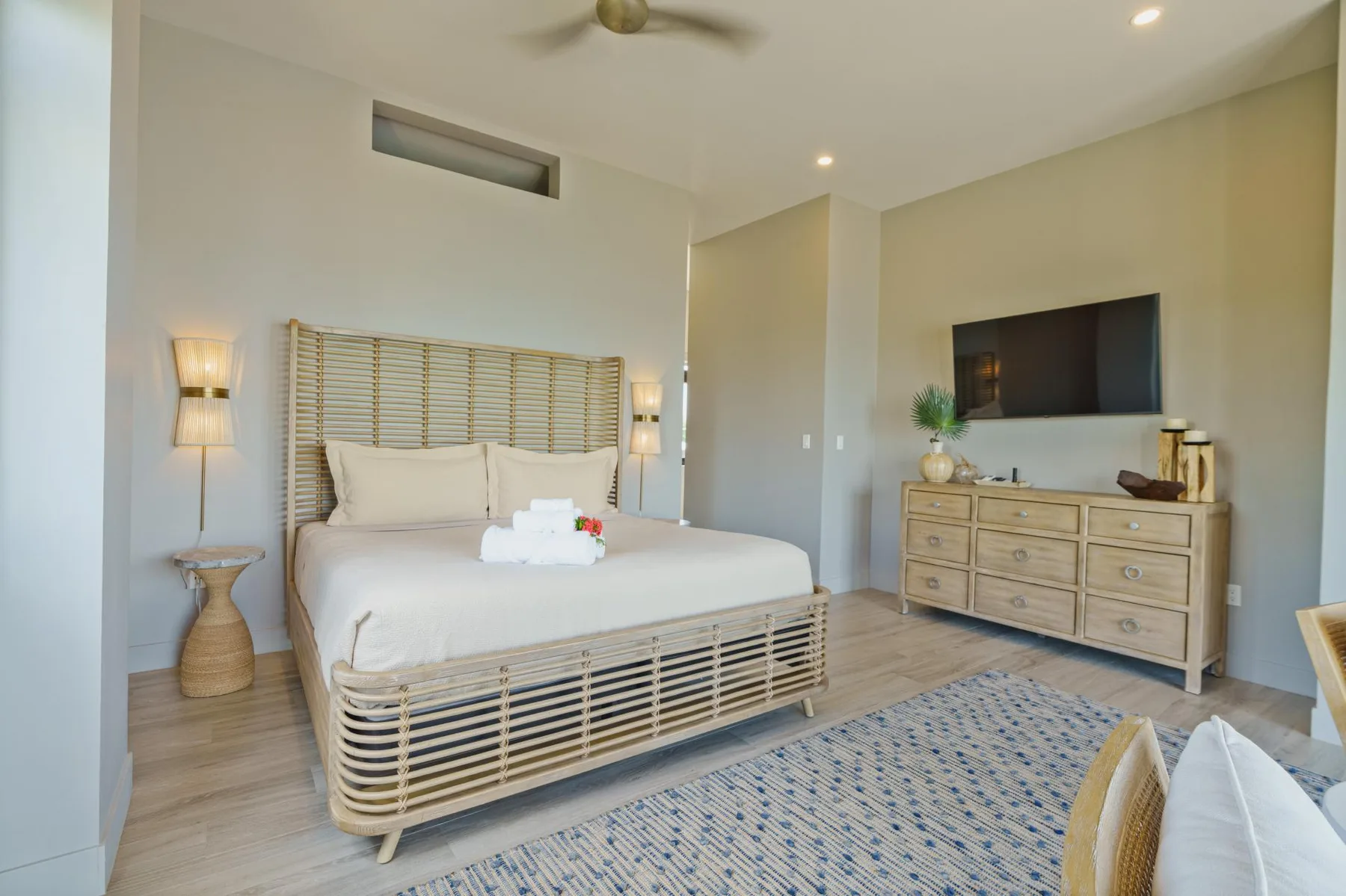 A bright bedroom with a bed, bedside lamps, and a dresser beneath a wall-mounted television.