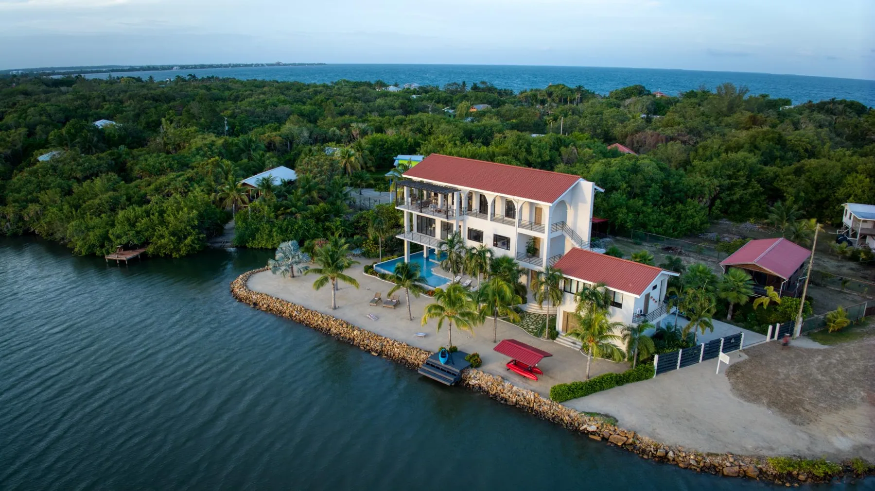 Aerial view of a waterfront property surrounded by trees, with the sea in the distance.