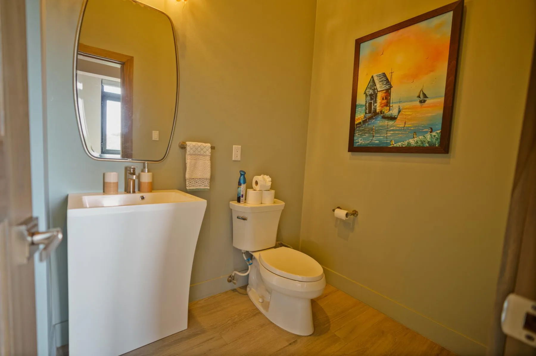 A bathroom with a sink, toilet, and framed seaside painting.