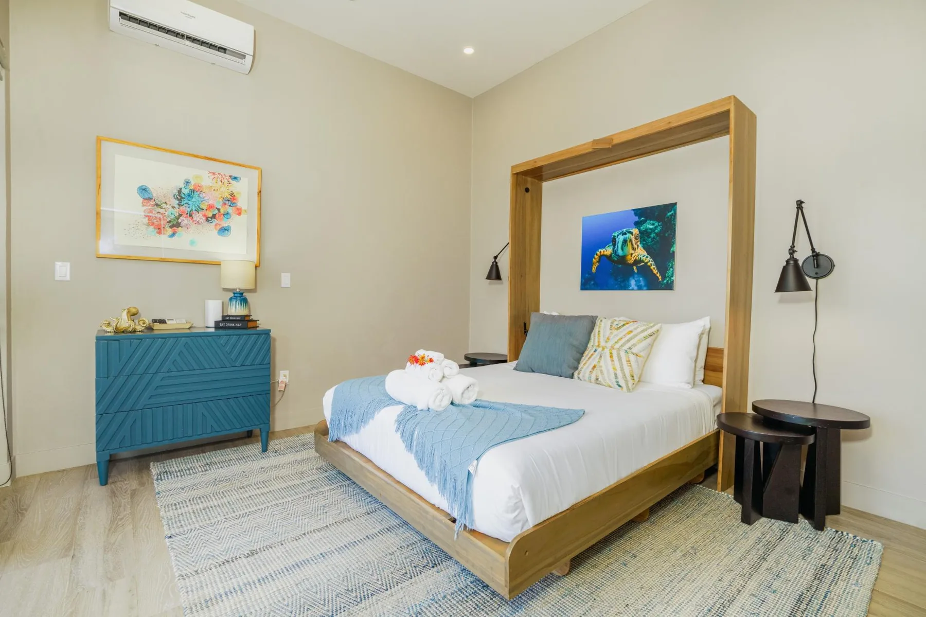A bedroom with a wooden-framed bed, blue bedding, and colorful wall art.