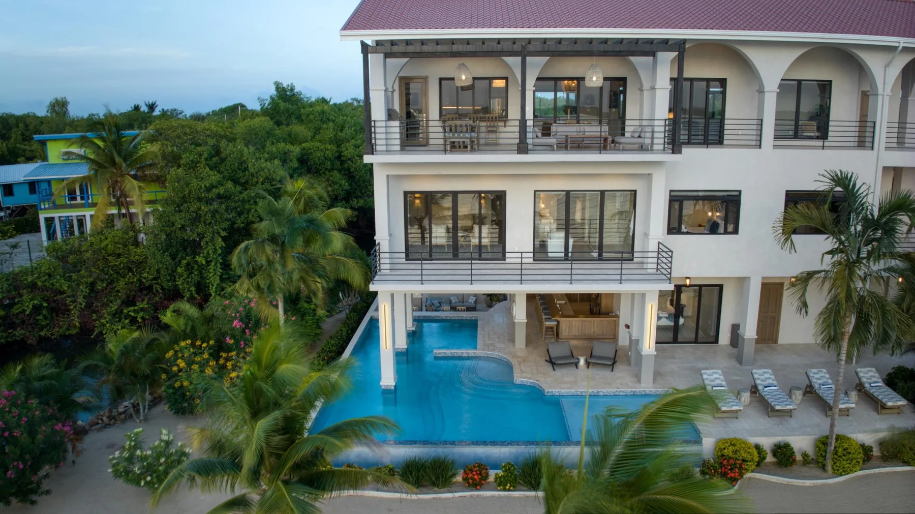 A multi-story building overlooks a swimming pool surrounded by greenery.