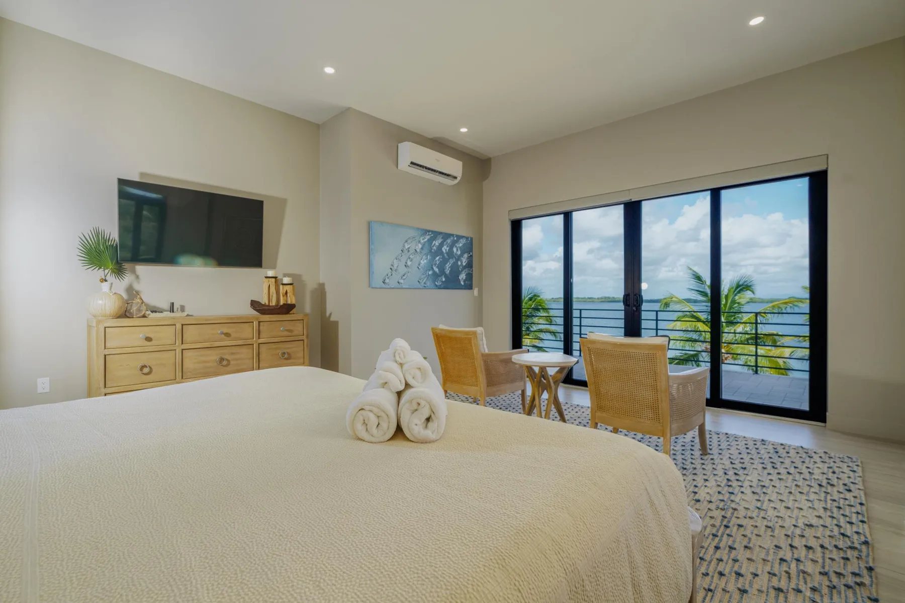 A bright bedroom with a bed, seating area, and glass doors opening to a balcony.