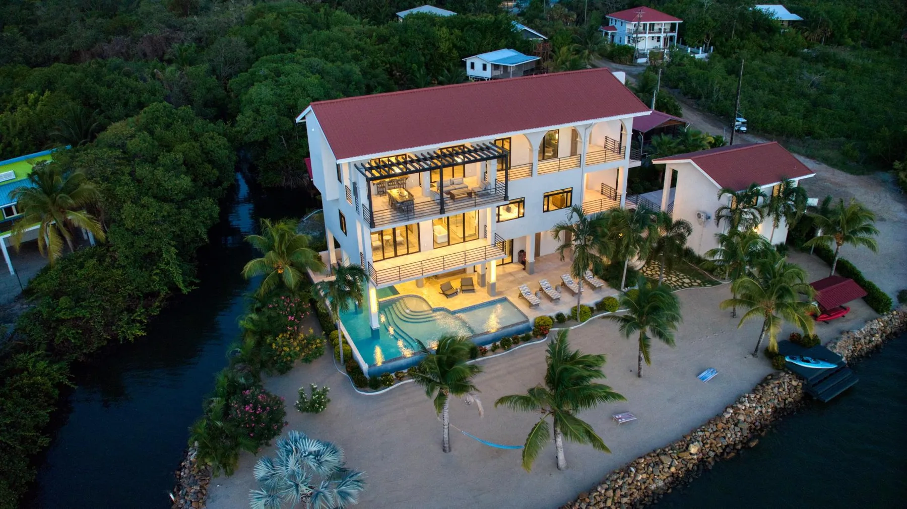 Aerial view of a lit beachfront building beside a sandy shore and palm trees.