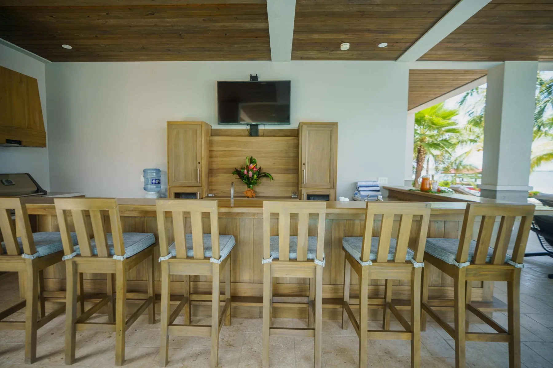 A wooden counter with high seating faces a wall-mounted television.