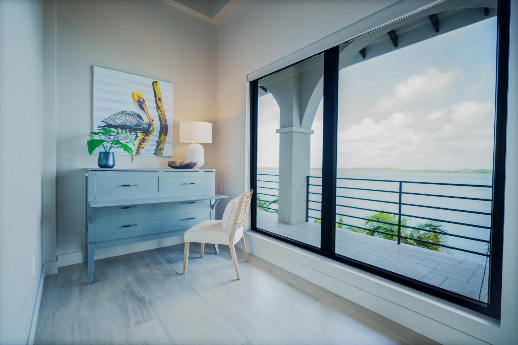 A bright room with a dresser and seating beside a large window overlooking the ocean.