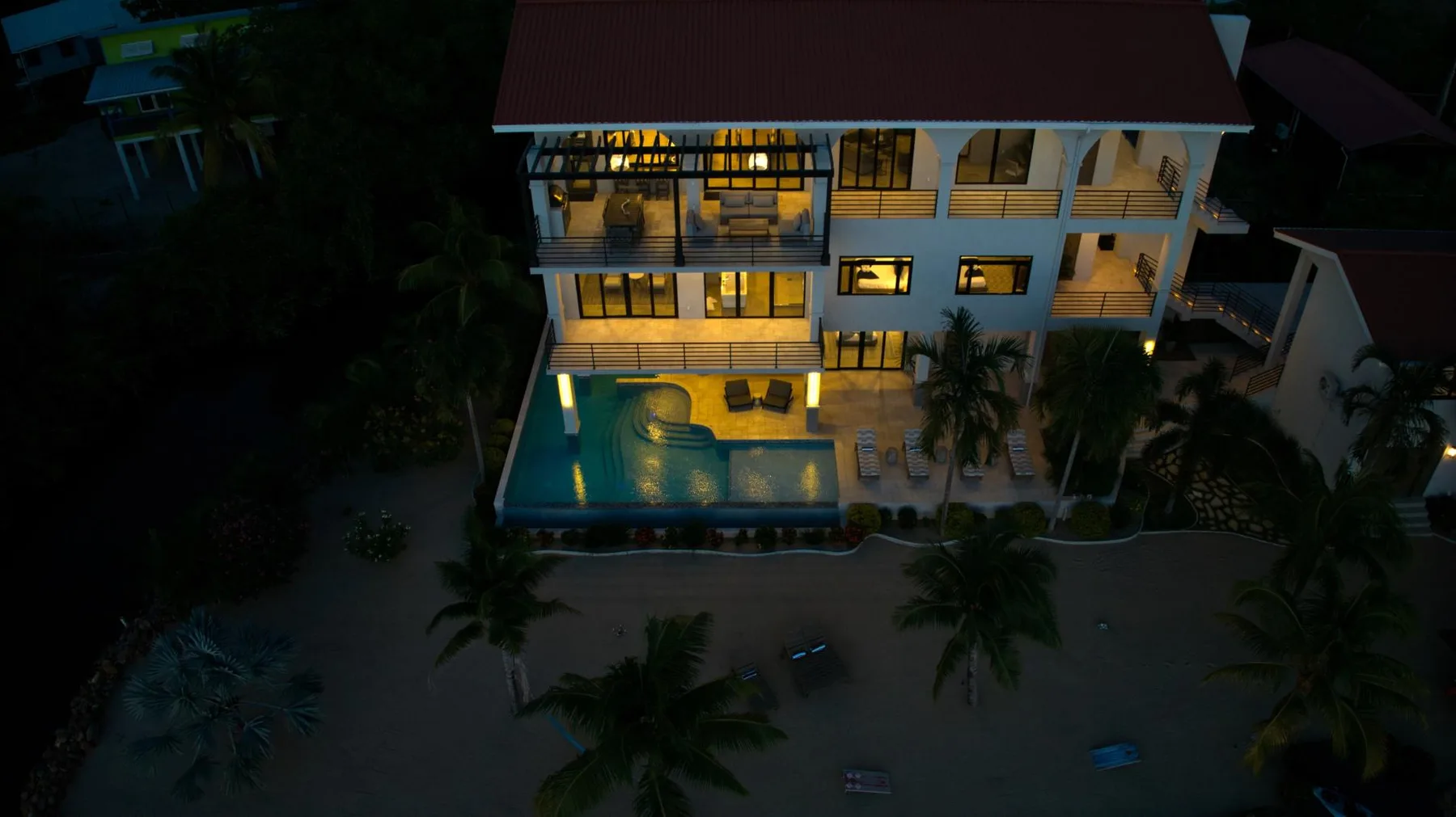 A large illuminated building stands beside a swimming pool at dusk.