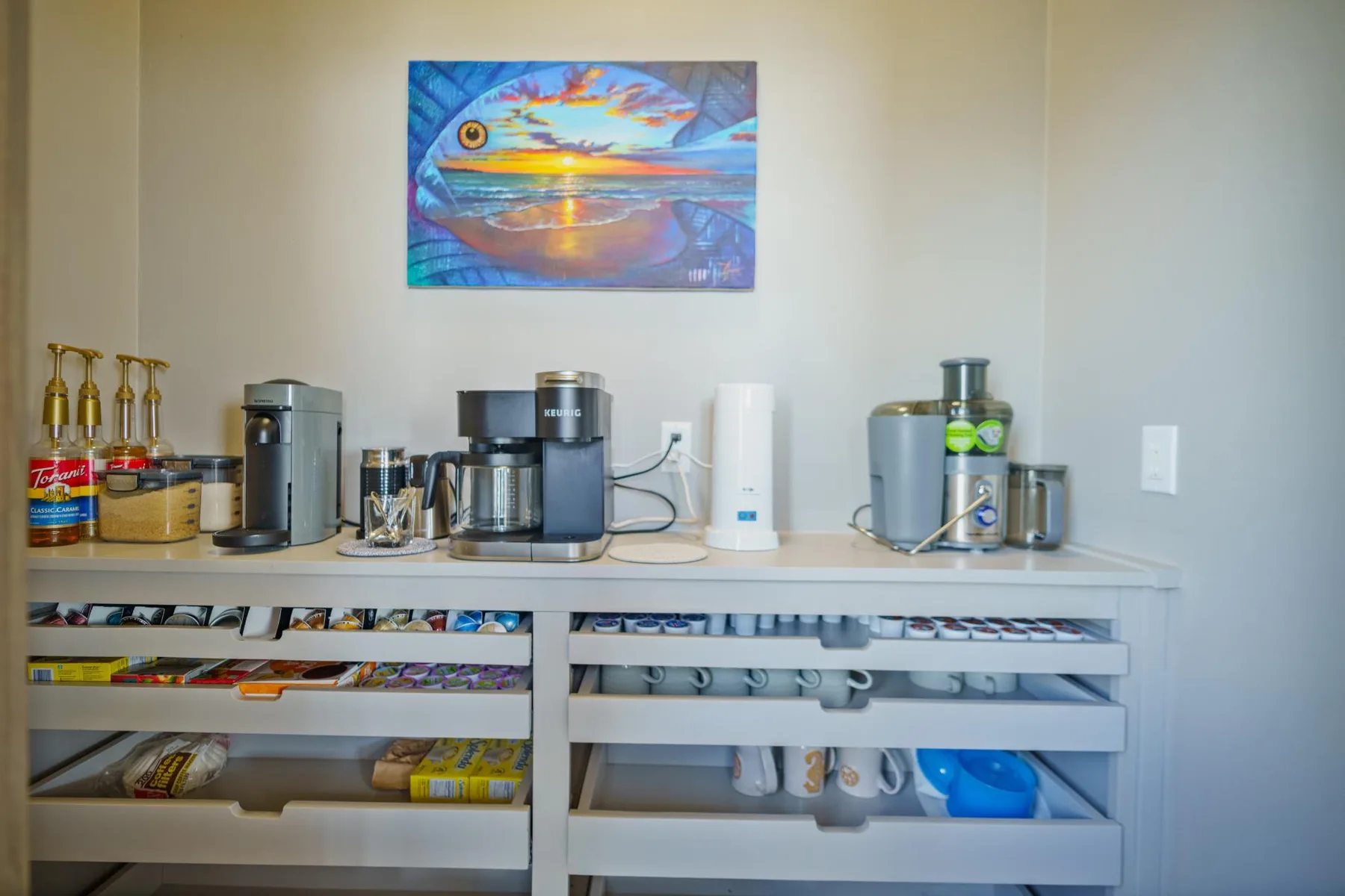A beverage station with coffee makers, drink supplies, and colorful wall art.