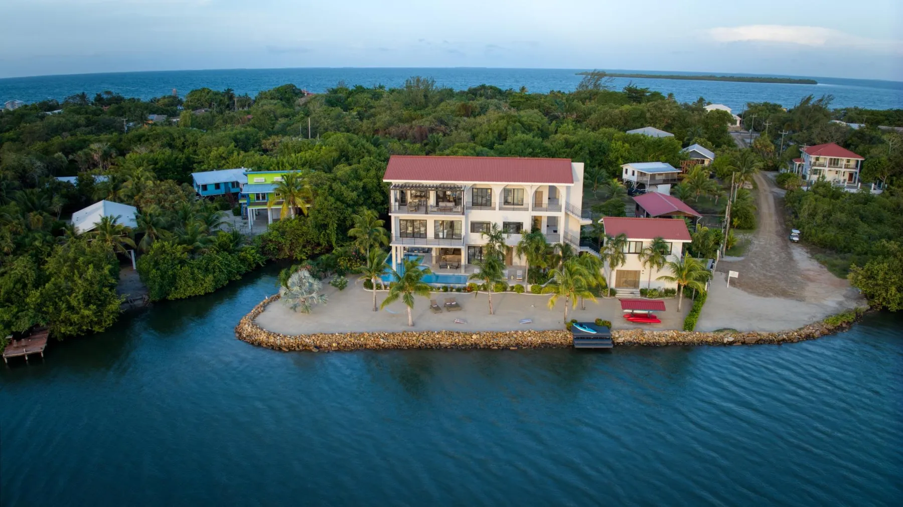 A waterfront building sits among trees beside a calm blue inlet.