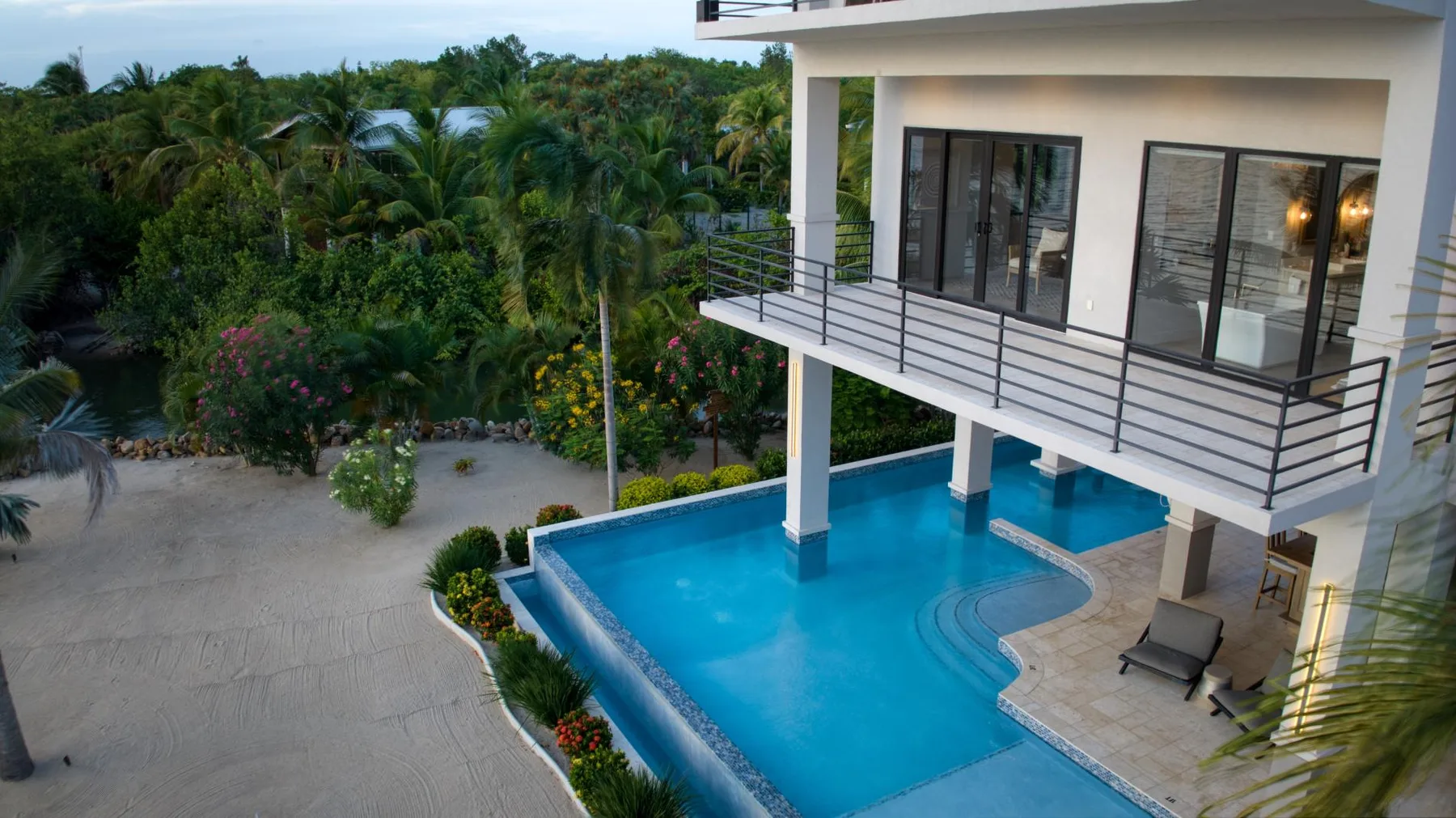 A modern building overlooks a blue swimming pool and lush tropical greenery.