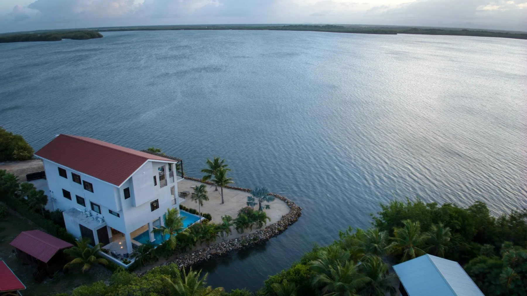 A white building beside a broad body of water, with a small landscaped shoreline.