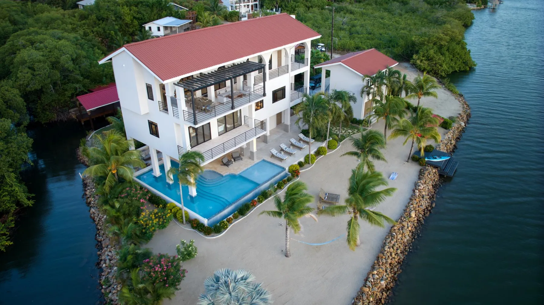 Aerial view of a waterfront house with a swimming pool and palm trees.
