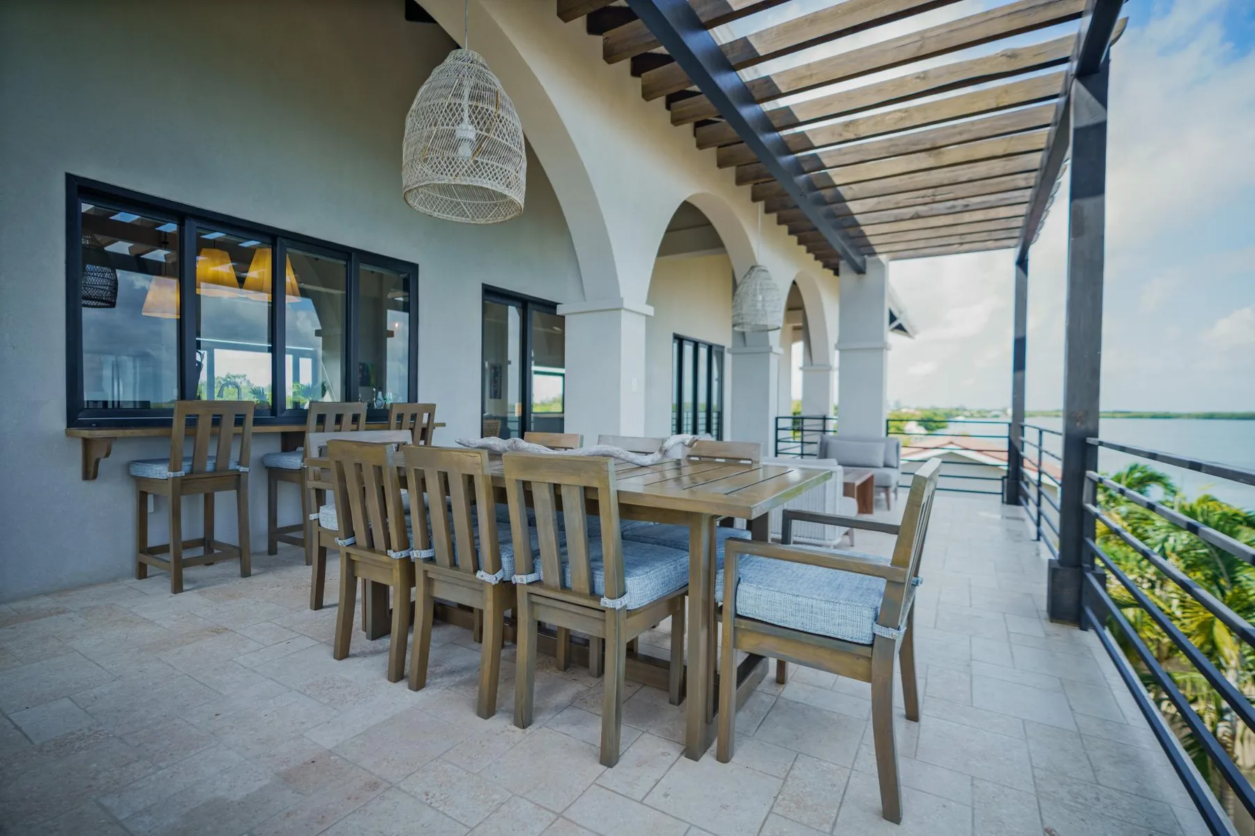 A covered outdoor dining area has wooden tables and chairs beside arched openings.