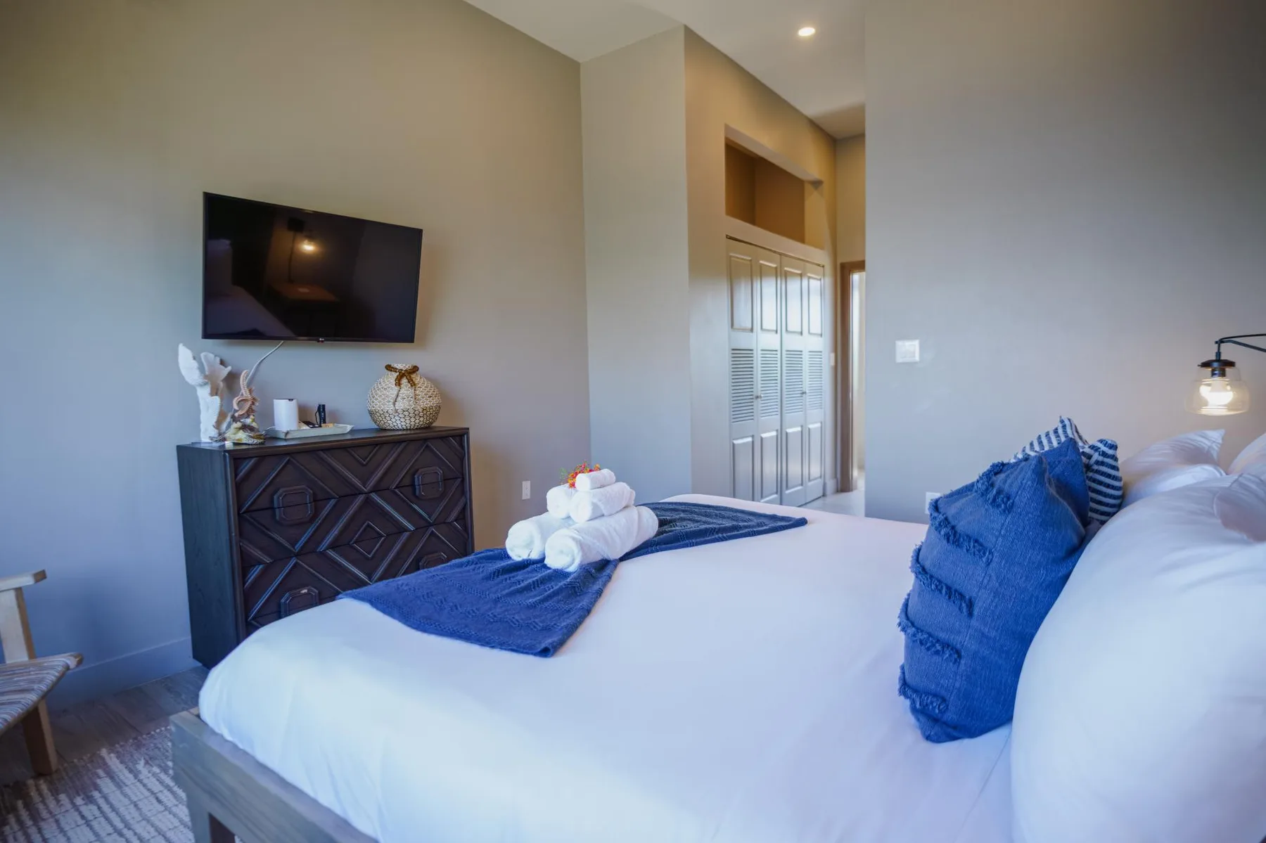 Bedroom with a neatly made bed, blue pillows, and a television above a dresser.