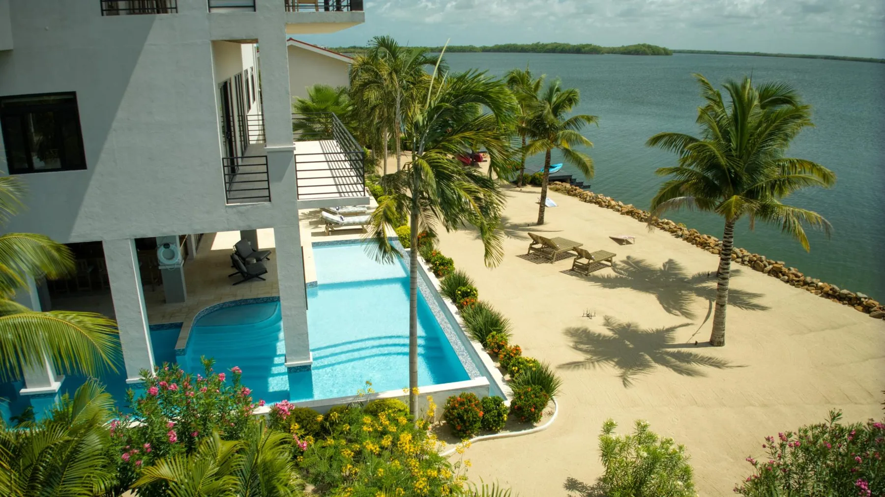 A waterfront pool and sandy beach sit beside a modern building.