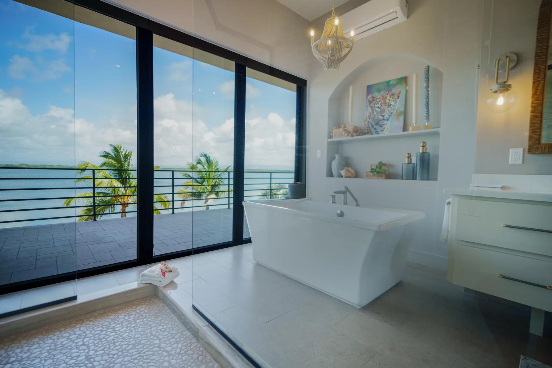 A bright bathroom with a freestanding bathtub beside large windows overlooking the sea.