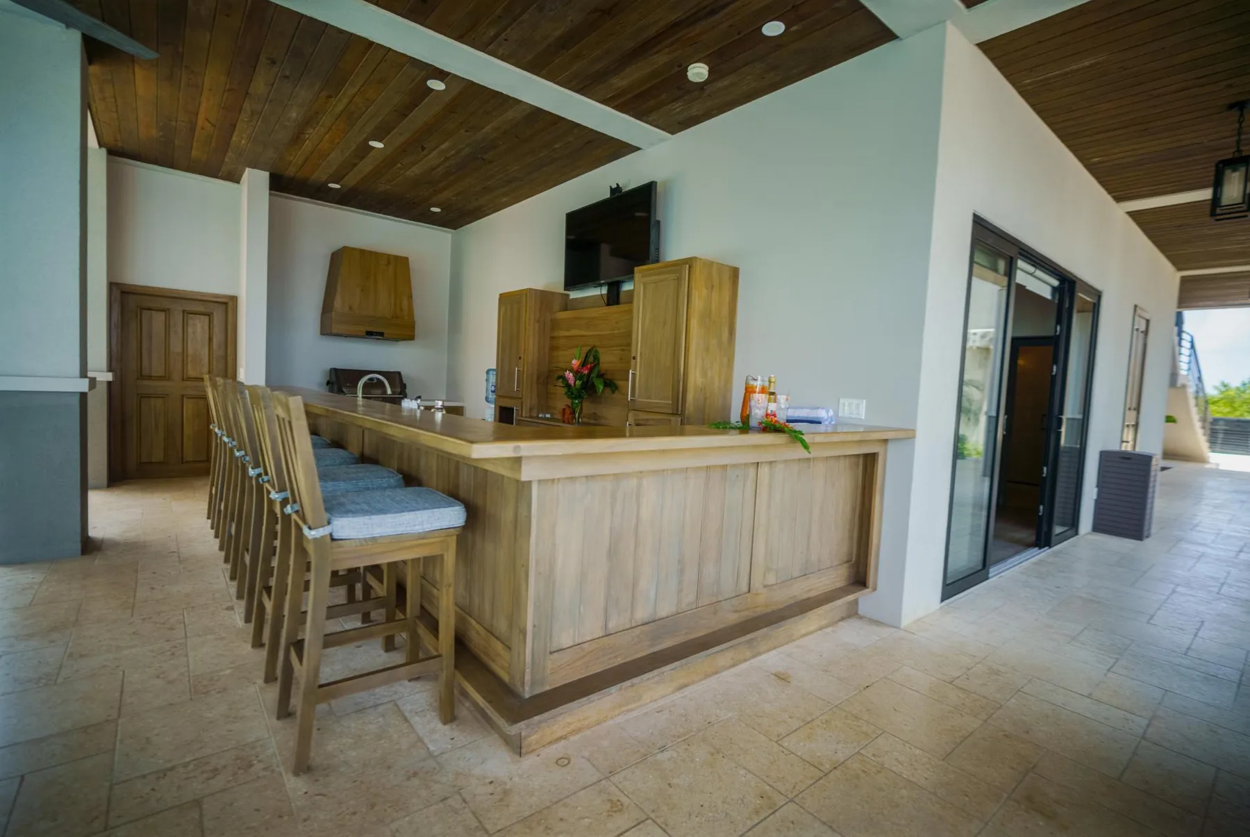 A wooden bar counter with stools sits in a covered open-sided area.