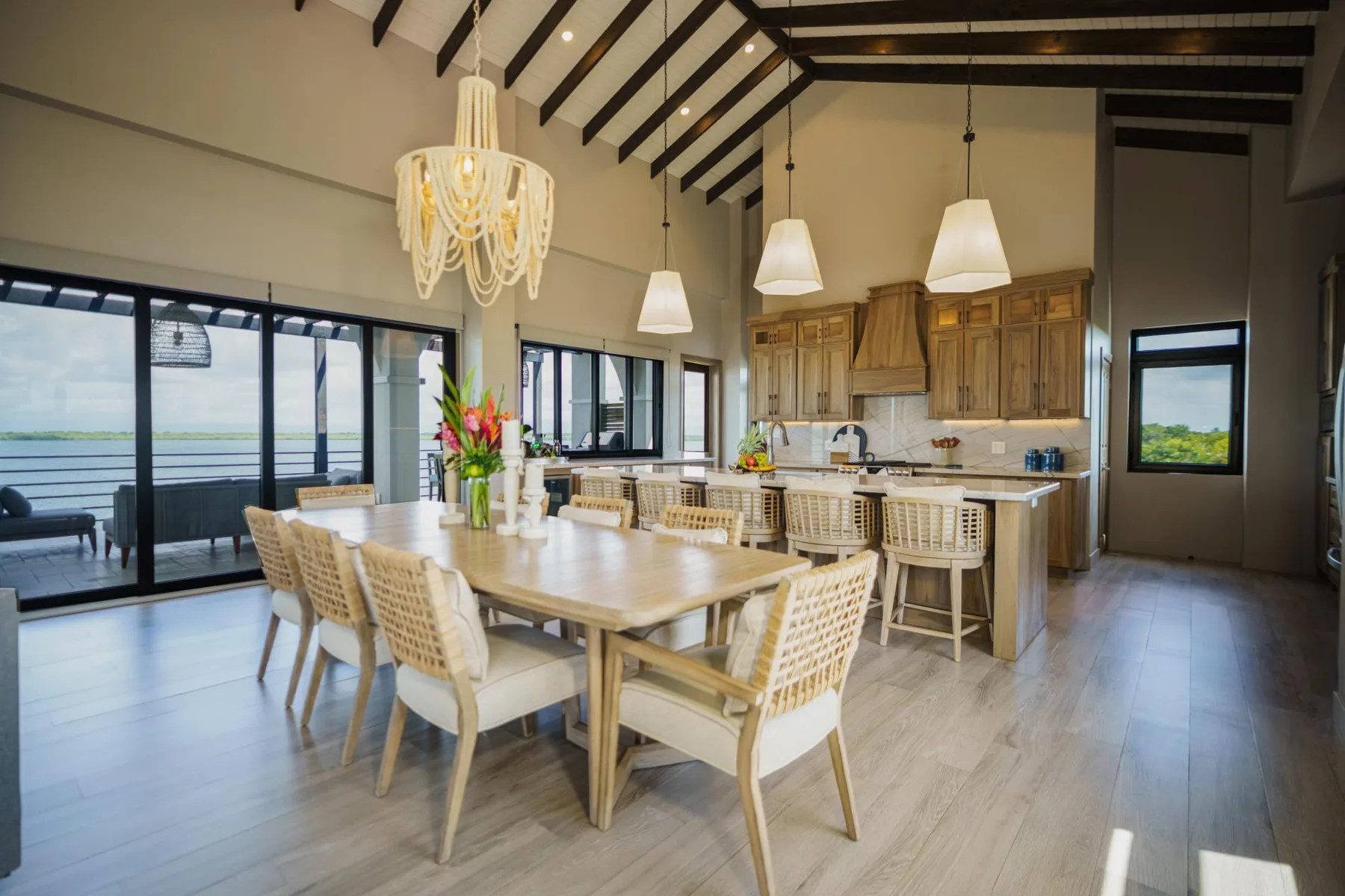 A dining area opens onto a kitchen, with a long table beneath exposed ceiling beams.