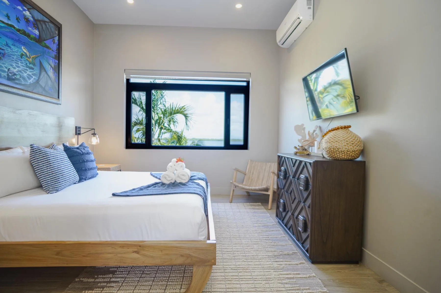 A bedroom with a neatly made bed and a window overlooking greenery.
