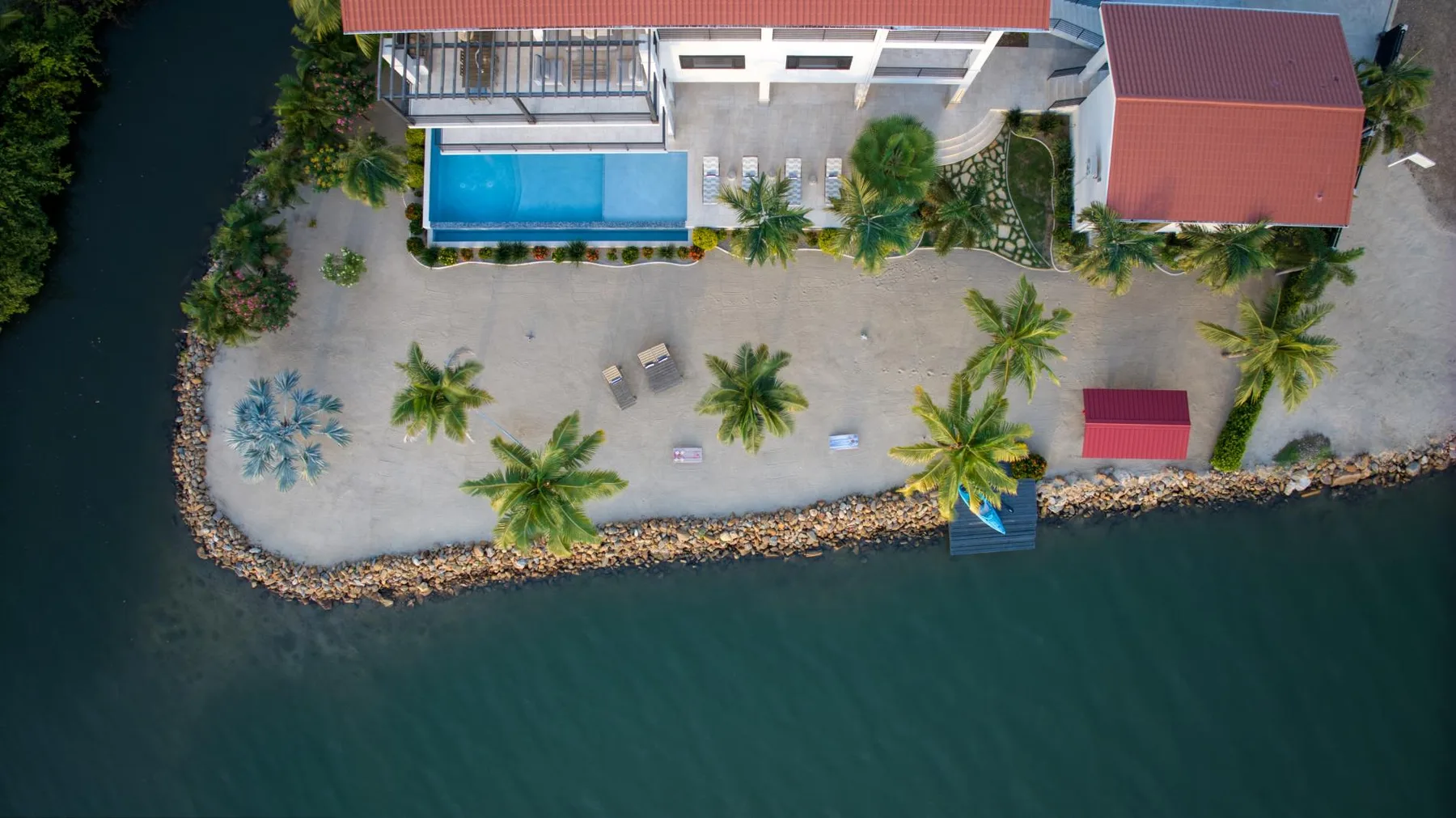 An aerial view shows a waterfront property with a swimming pool and palm trees.