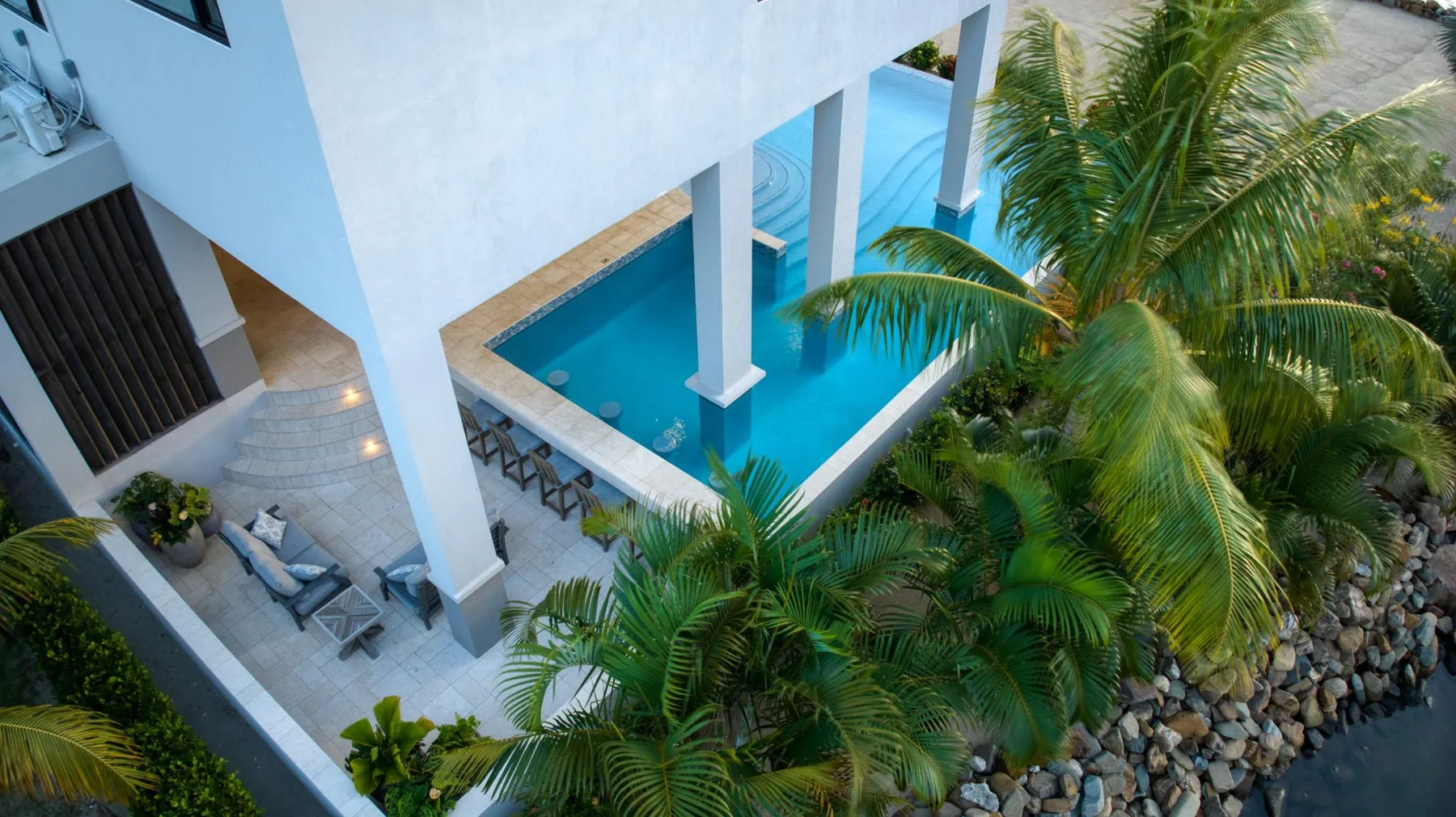 An outdoor pool beside a white building, surrounded by palm trees.