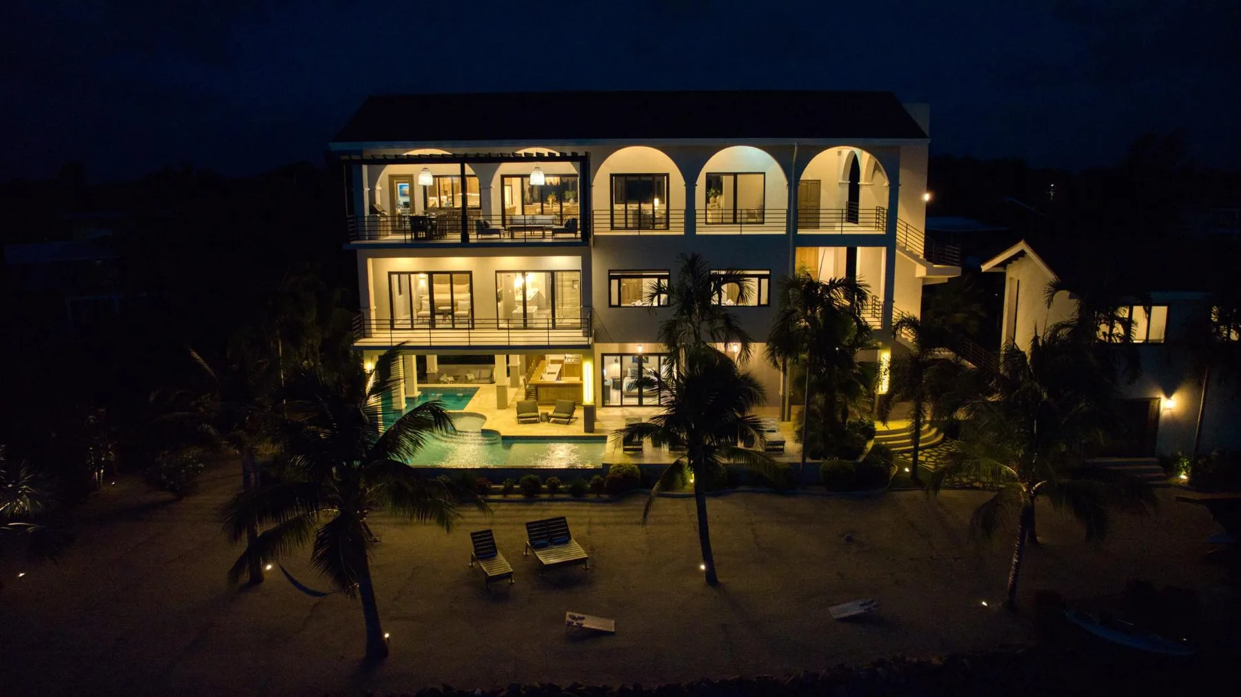 A multi-story building glows at night beside a lit swimming pool.
