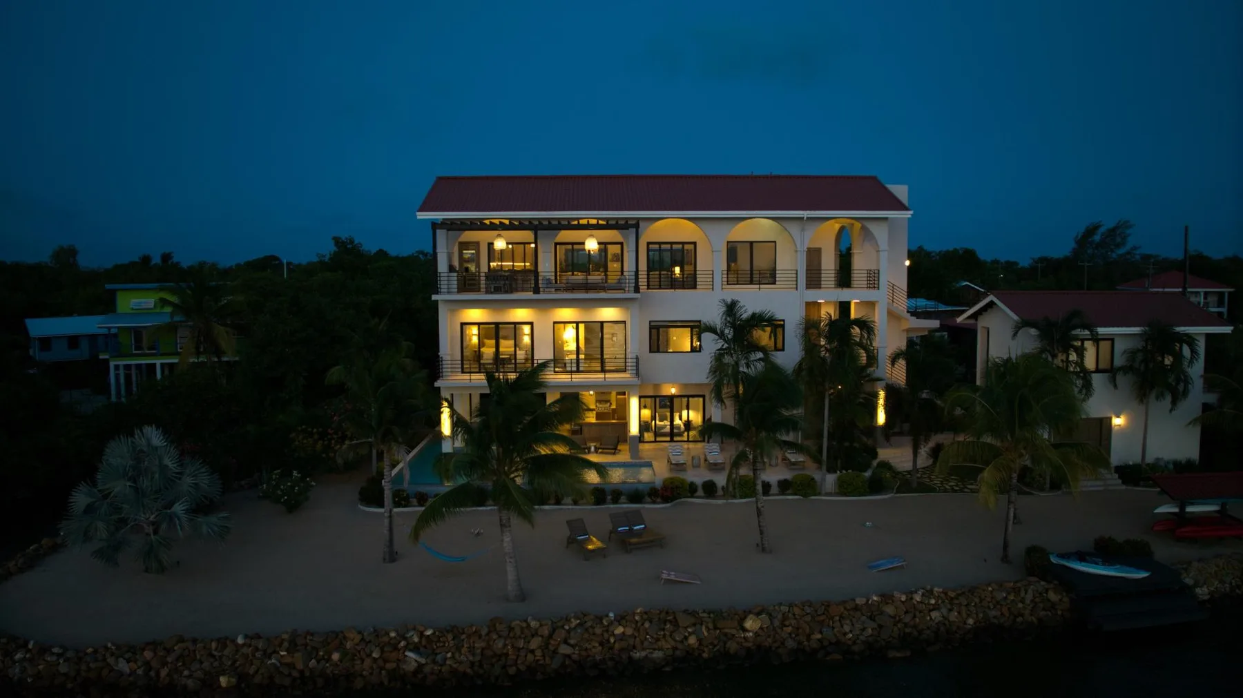 A multi-story building with illuminated balconies stands beside a waterfront at dusk.