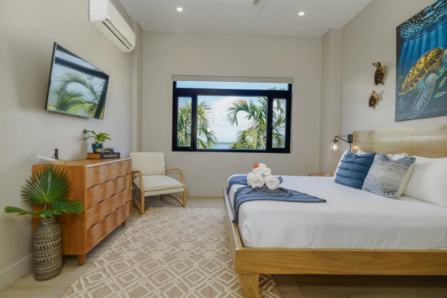 A bright bedroom with a neatly made bed and a window overlooking palm trees.