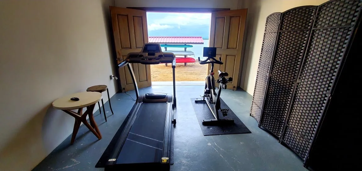 A small workout room with exercise machines beside open doors to an outdoor deck.
