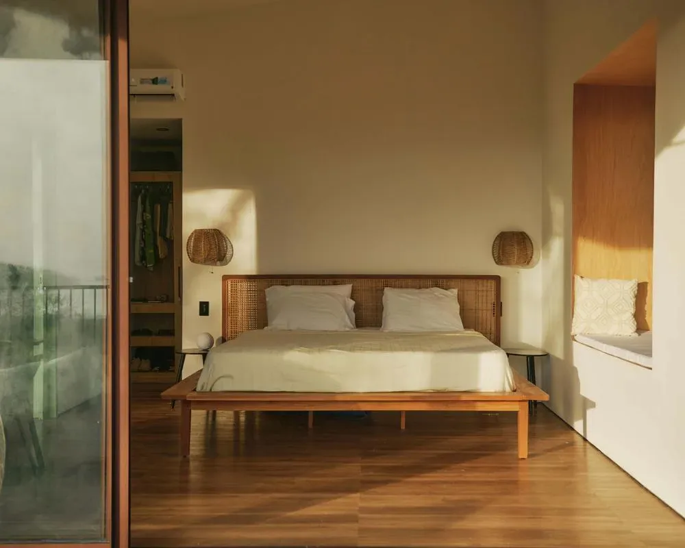 A bedroom with a bed centered against the wall and warm sunlight across the floor.