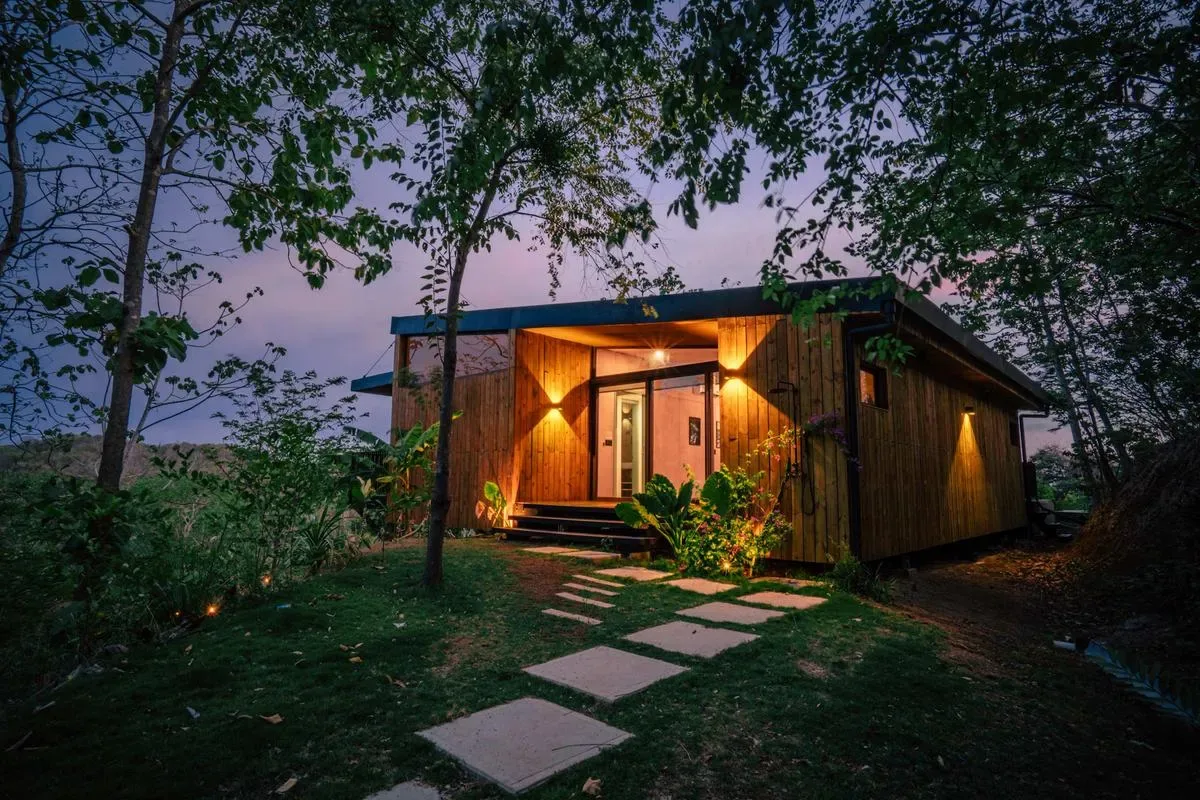 A small wooden cabin glows among trees beside a path of stepping stones.