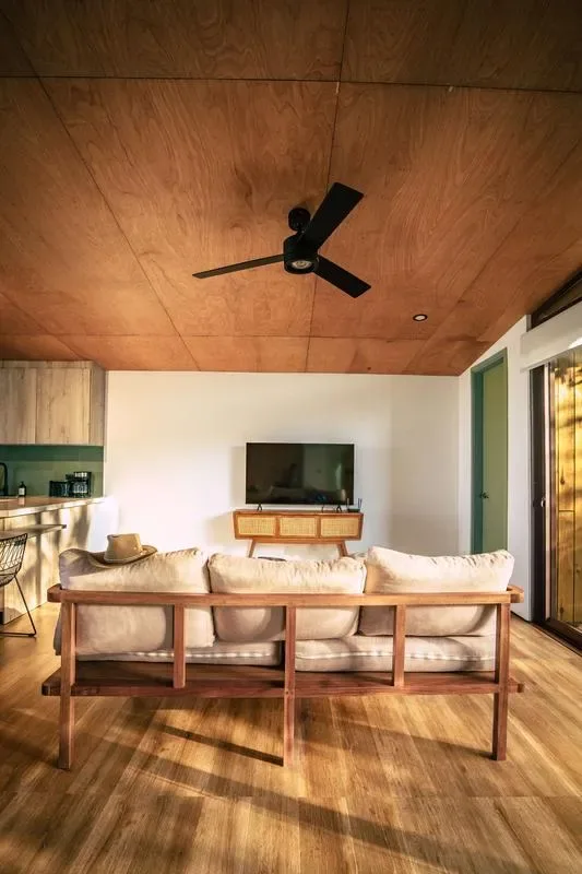 A living room with a sofa facing a television beneath a wood-paneled ceiling.