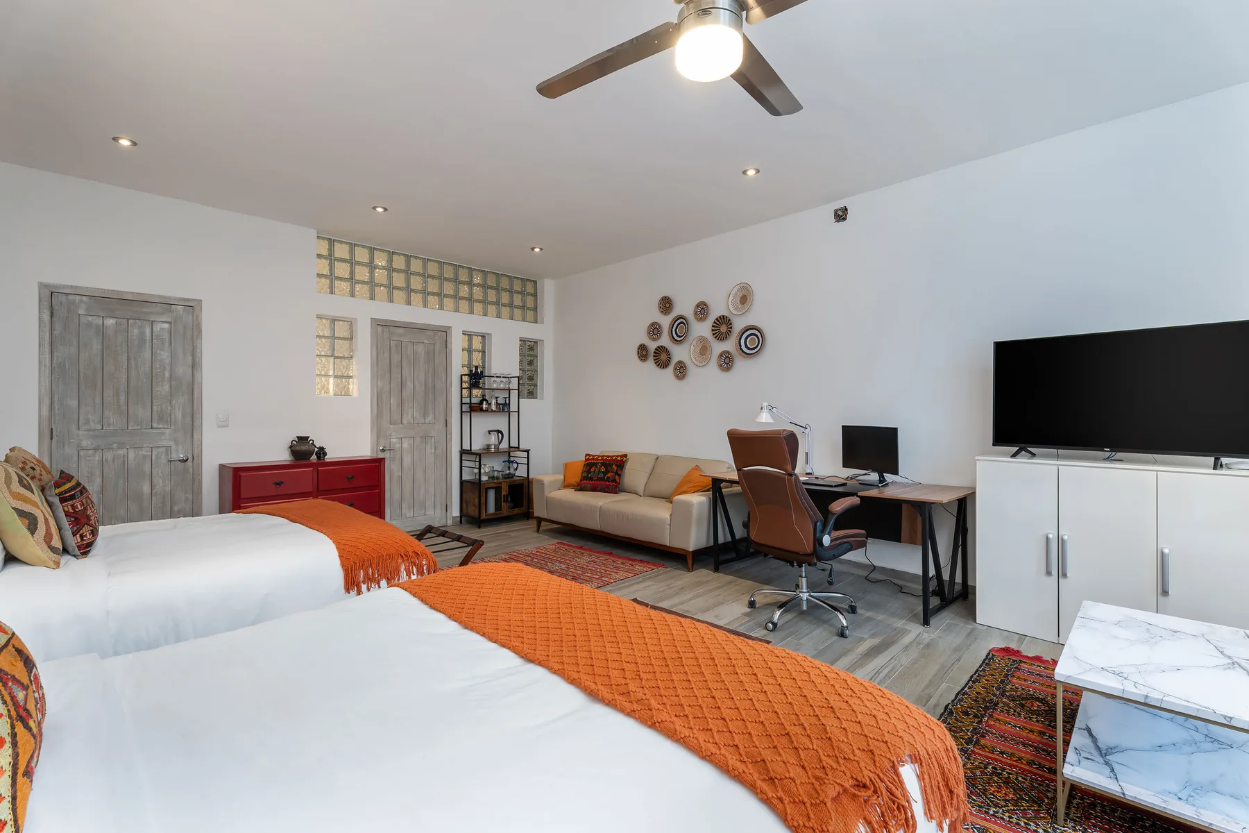 A bright bedroom with two beds, a desk, and a television.
