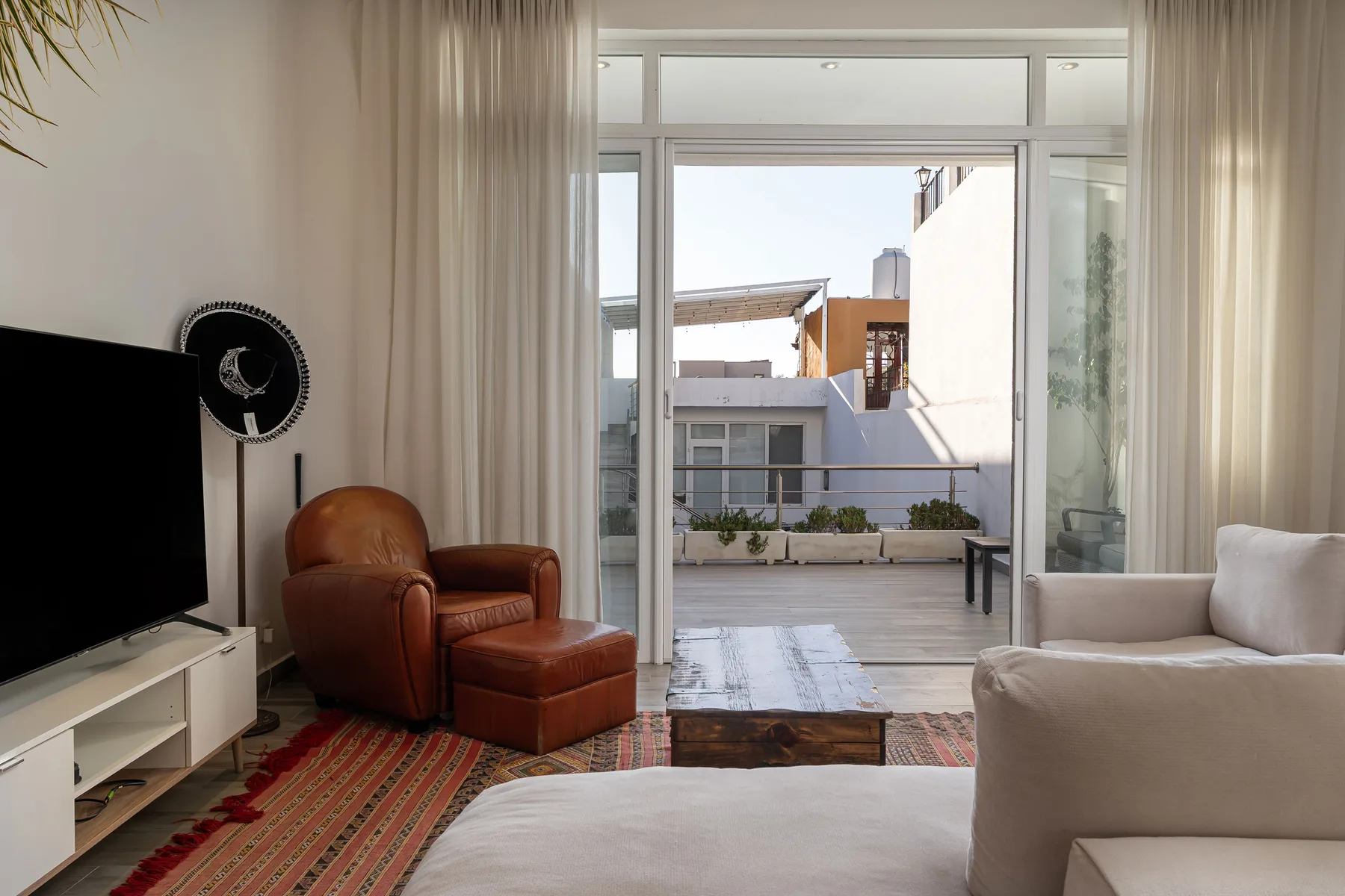 A bright living room opens onto a balcony through large glass doors.