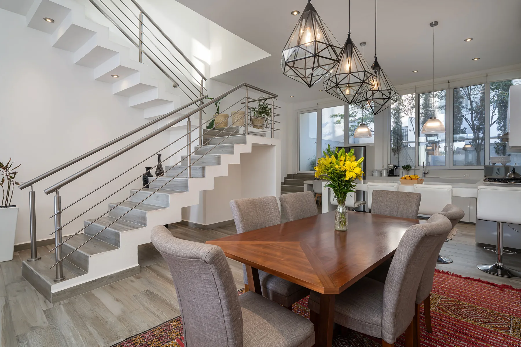 An open dining and living area features a wooden table beneath geometric pendant lights.