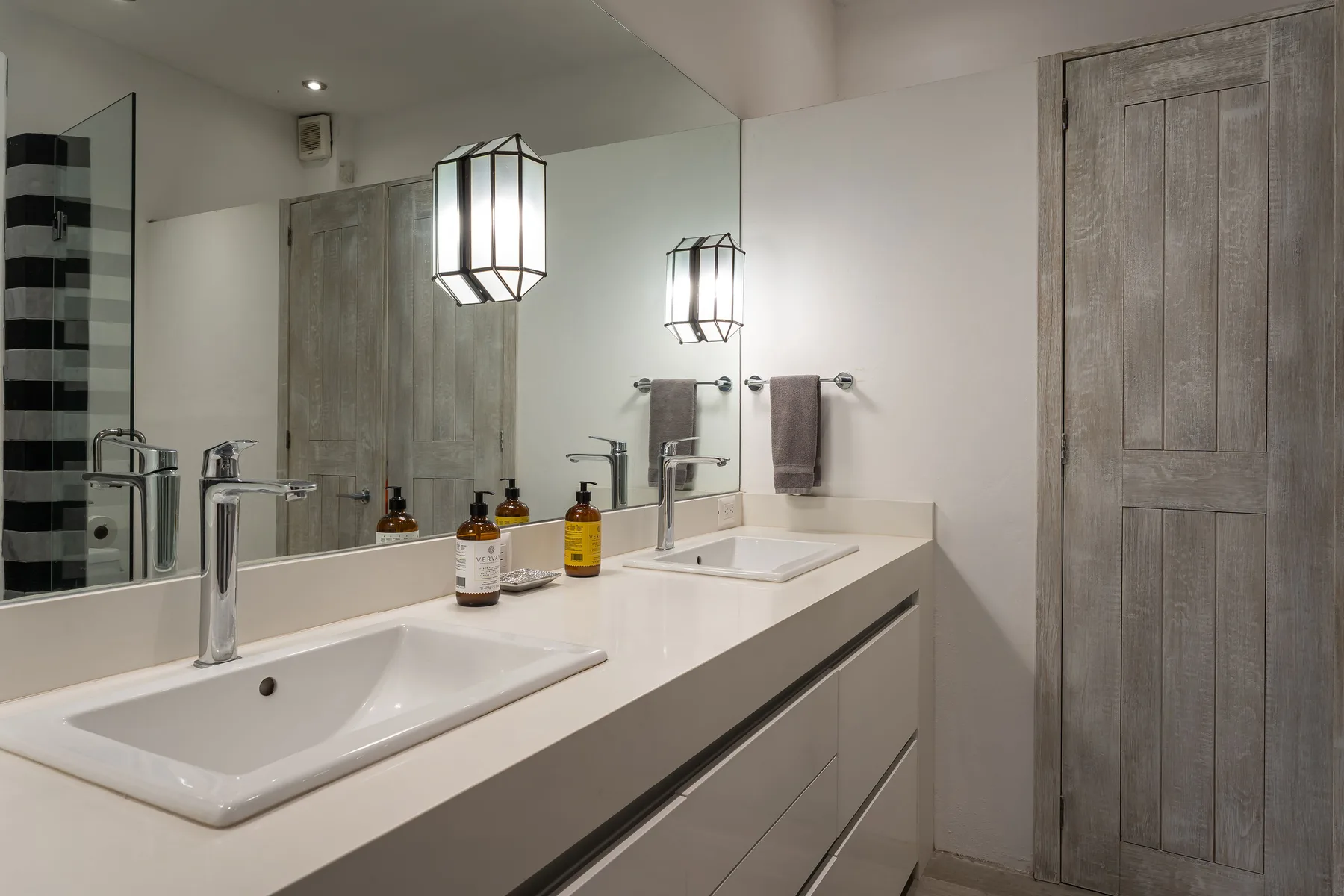 A bathroom vanity with two sinks, mirrors, and pendant lights.
