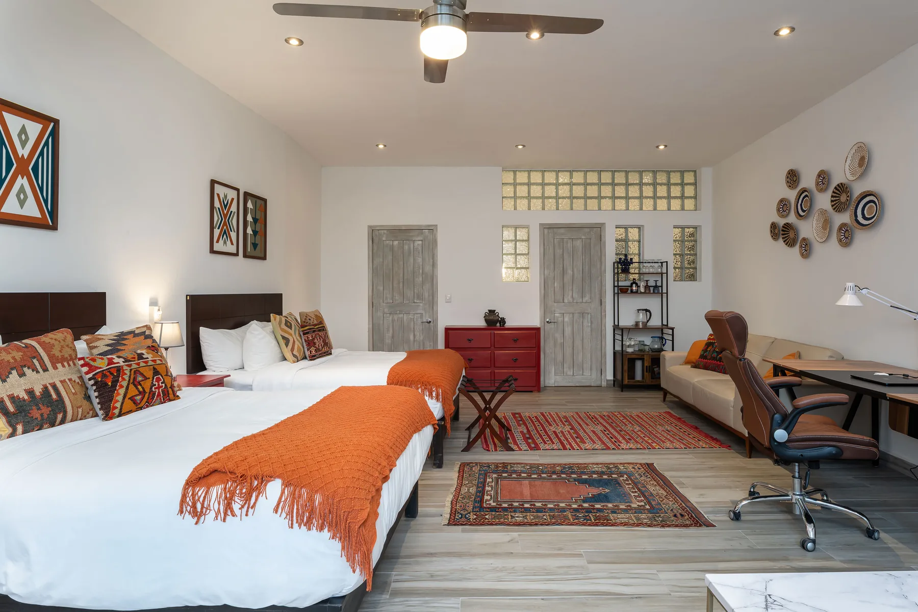 A bedroom with two beds, patterned rugs, and a desk along the wall.